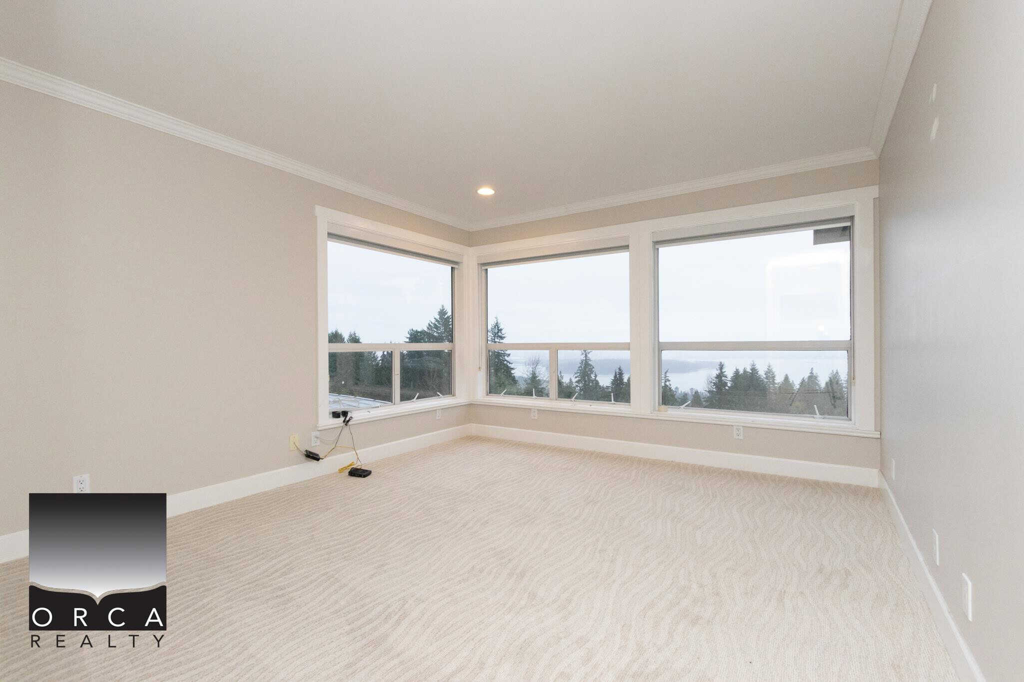 Spacious bright living room with large windows offering beautiful mountain and ocean views, featuring neutral walls and plush carpet, ideal for modern home interiors and real estate showcasing.