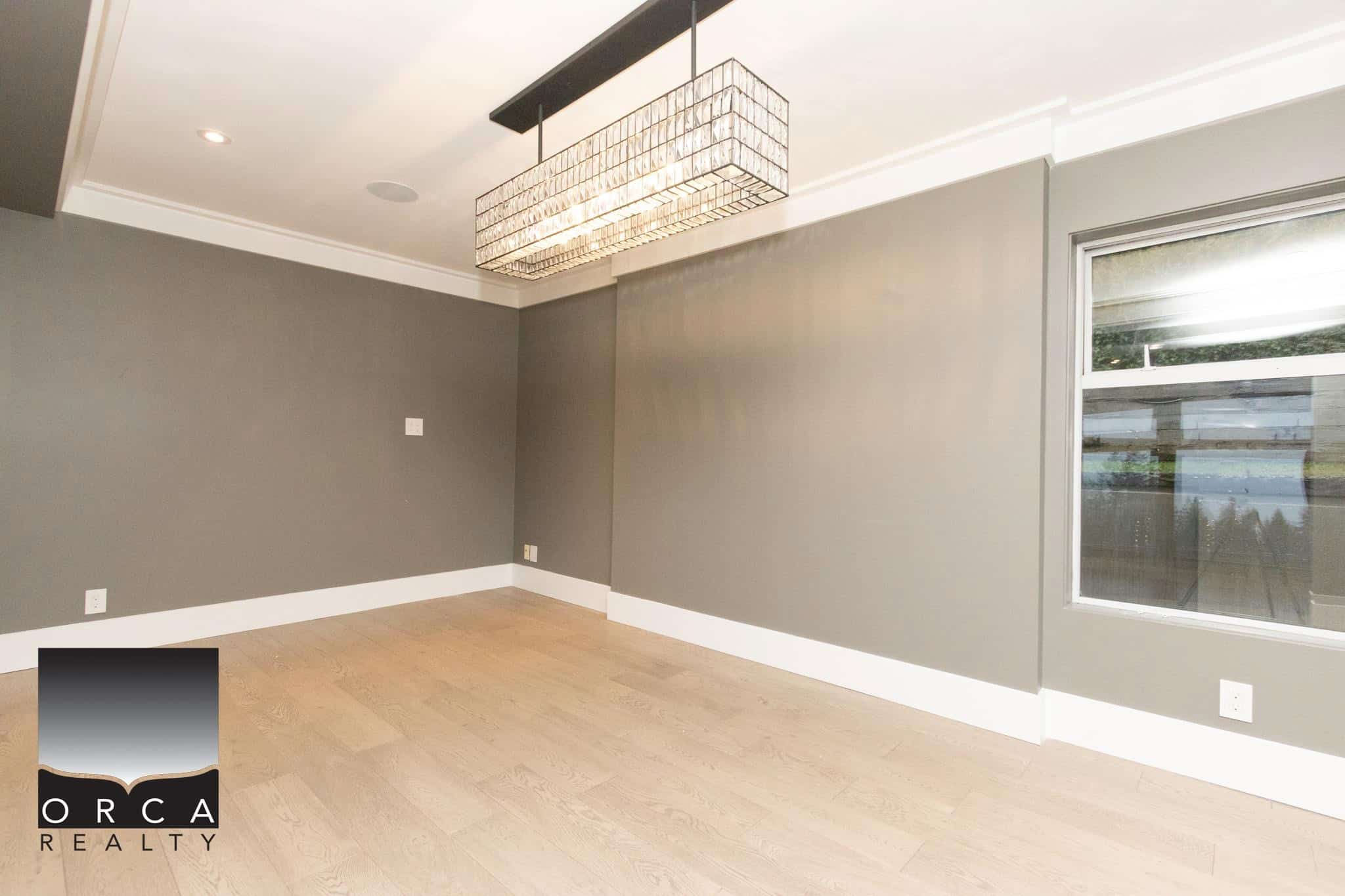 Bright modern room with grey walls, natural hardwood flooring, large window, and stylish ceiling pendant light, ideal for real estate decor and home staging by Orca Realty Inc.