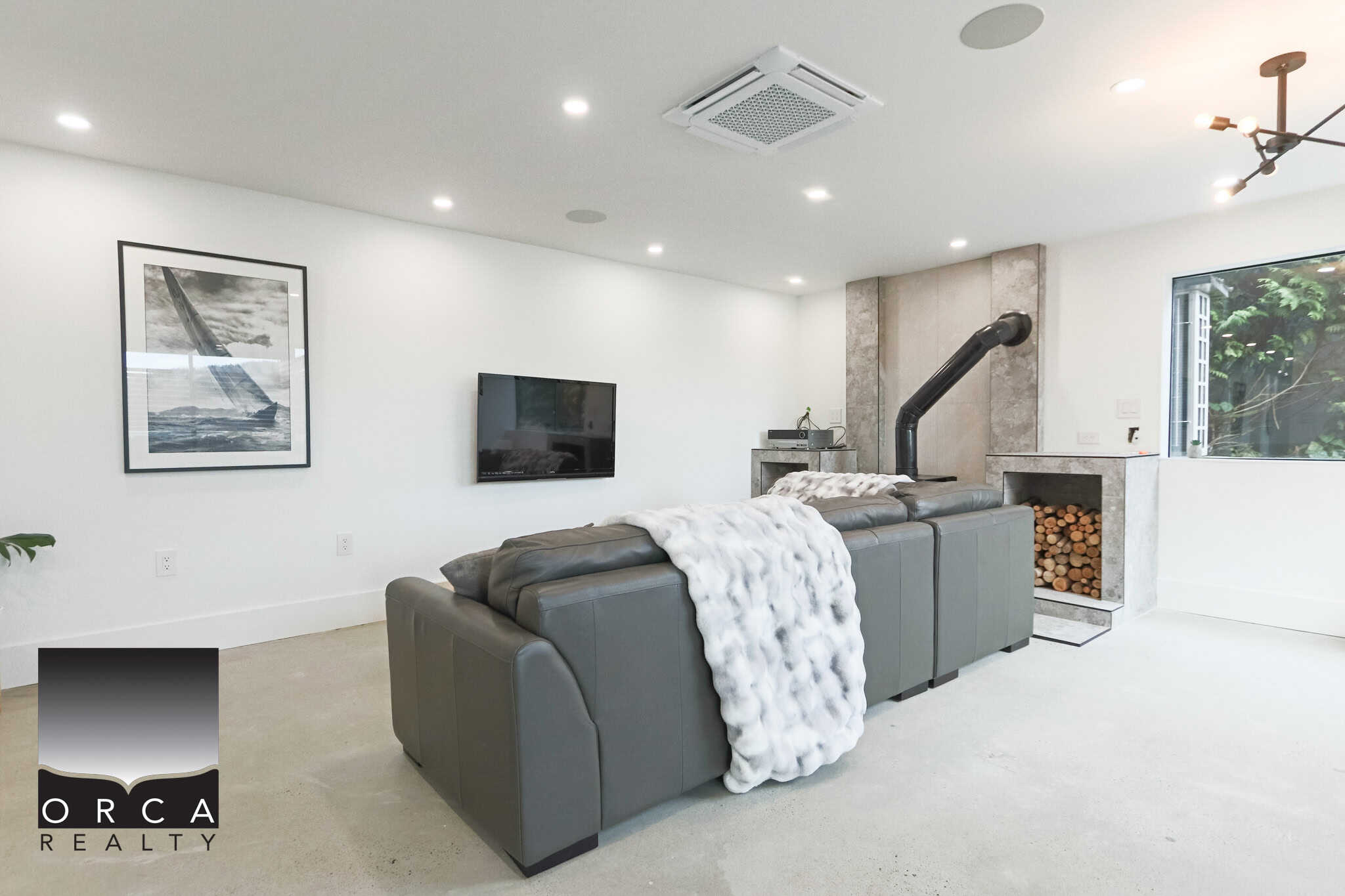 Stylish modern living room featuring a cozy gray leather sectional, contemporary fireplace with stacked firewood, and minimalist decor, ideal for Vancouver real estate listings and home showcase.