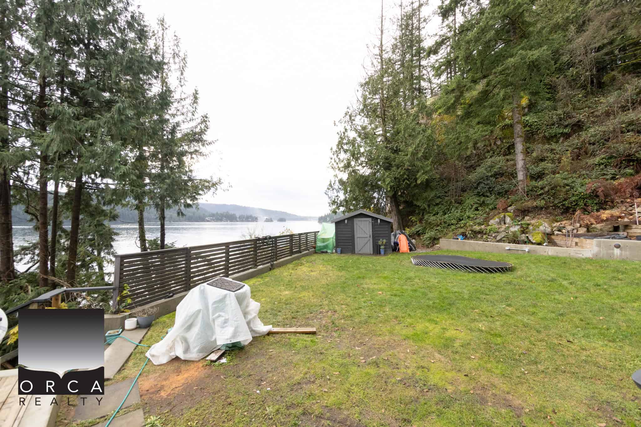 Lakeside backyard with lush green grass, mature trees, and a view of the water, perfect for outdoor living and enjoying nature. Ideal for real estate listings showcasing waterfront properties in BC.