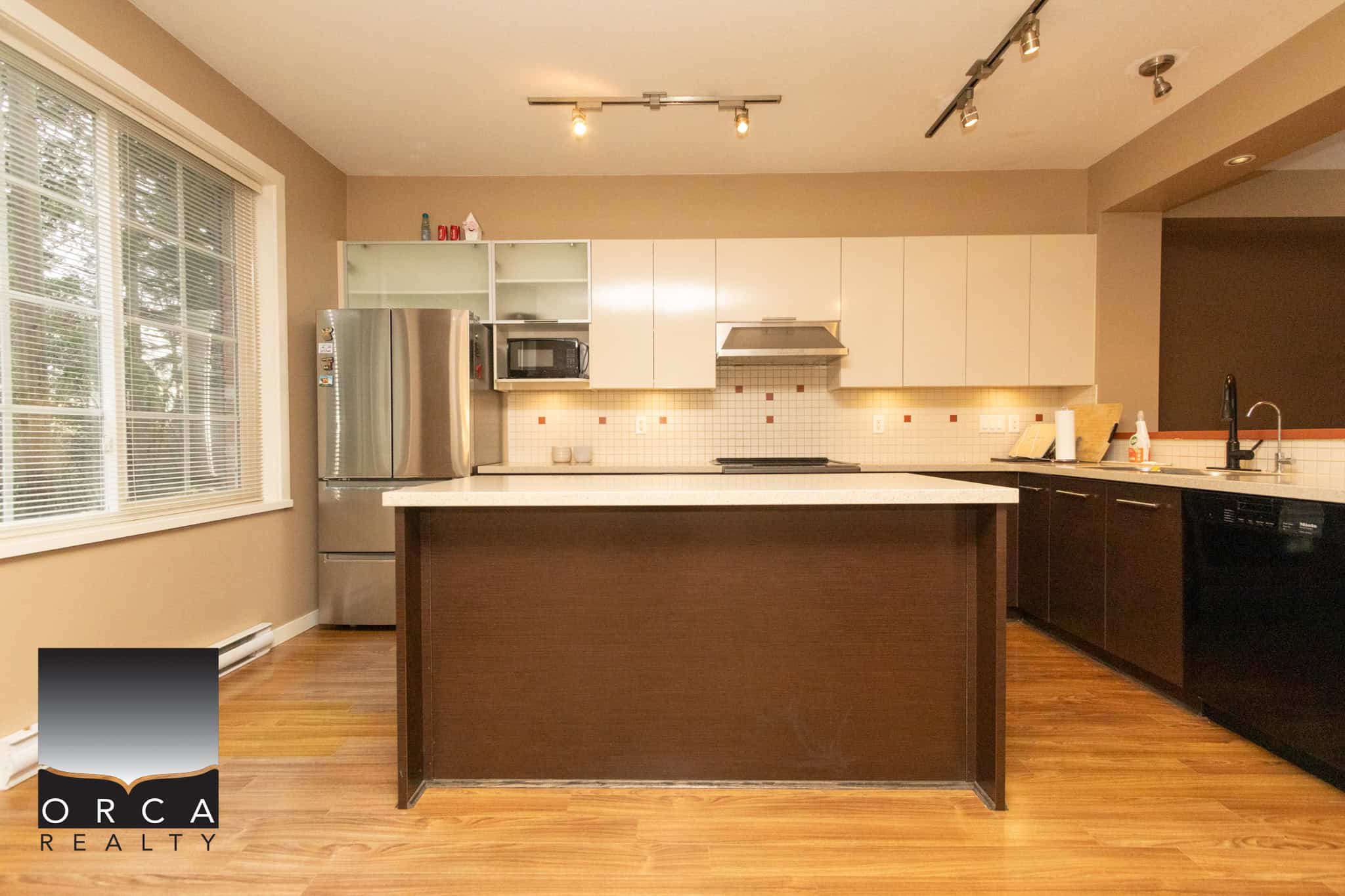 Bright modern kitchen with stainless steel appliances, white cabinetry, and a spacious island, ideal for family living and entertaining in a beautifully maintained Orca Realty Inc. property in BC.