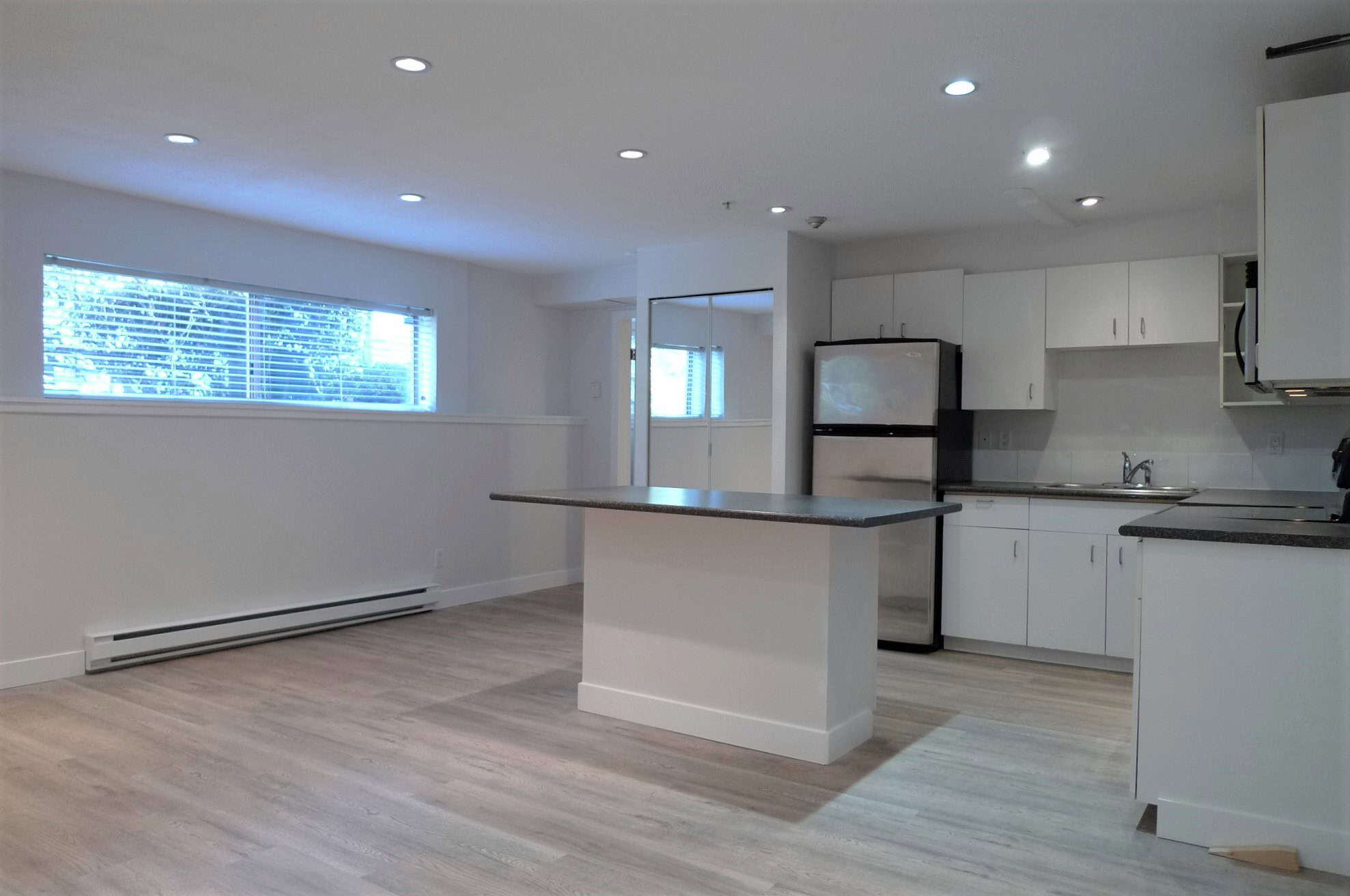 Bright open kitchen with white cabinetry, stainless steel appliances, and ample natural light in a modern condo, perfect for convenient living in the Vancouver area by Orca Realty Inc.