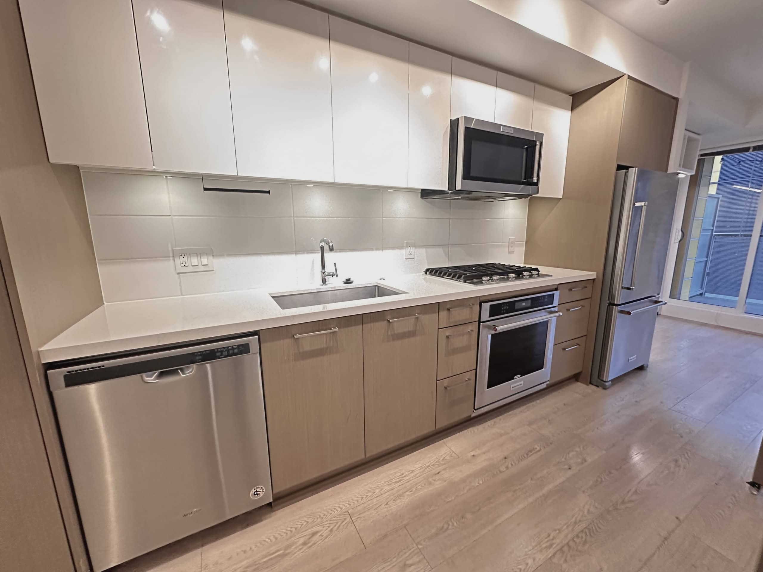 Modern stainless steel kitchen appliances including a refrigerator, oven, microwave, and dishwasher in a contemporary condo or apartment, featuring sleek cabinetry and hardwood floors.