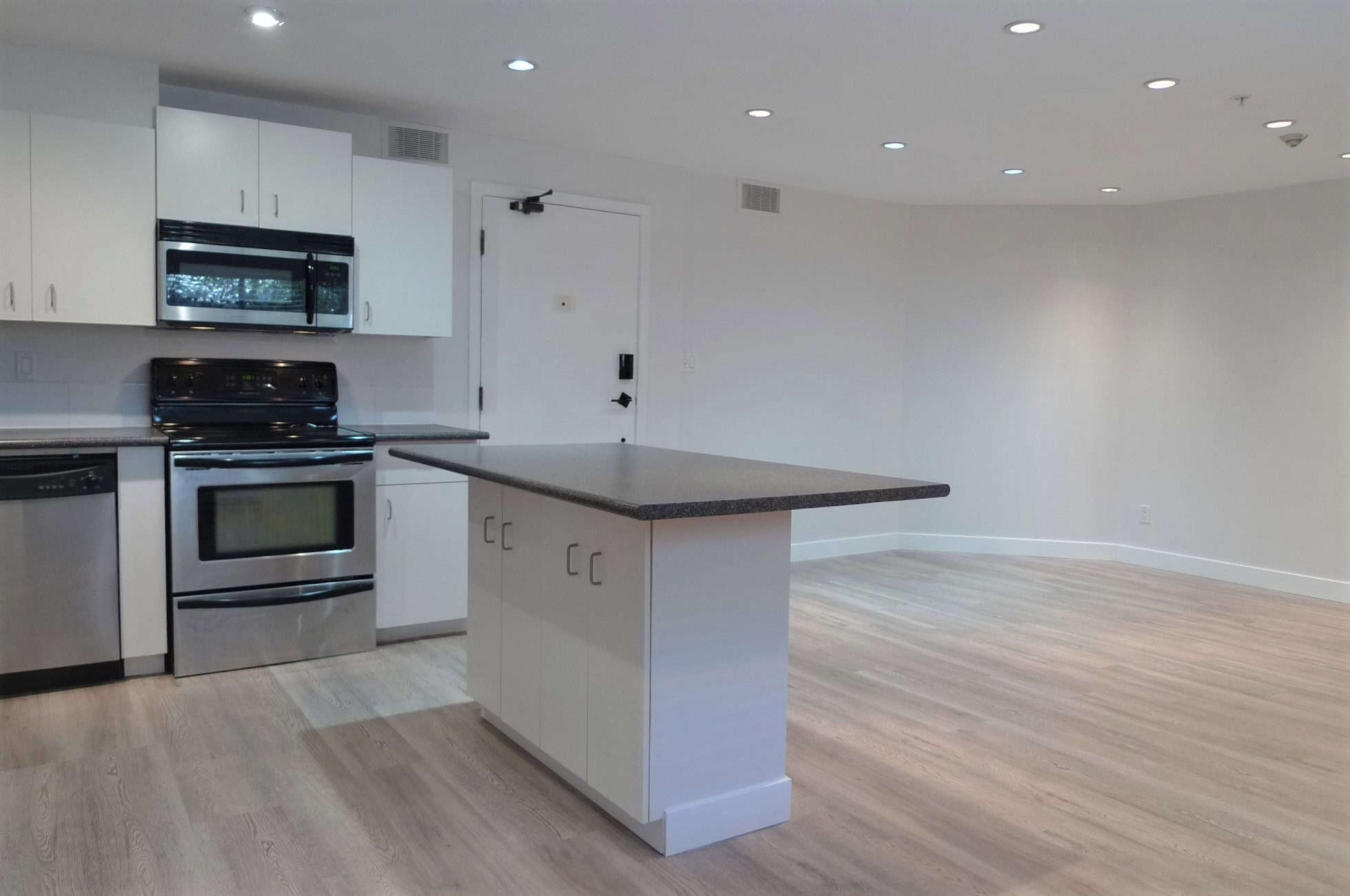 Bright modern kitchen with white cabinets, stainless steel appliances, and a central island, perfect for Vancouver Island real estate buyers seeking stylish, functional home features.