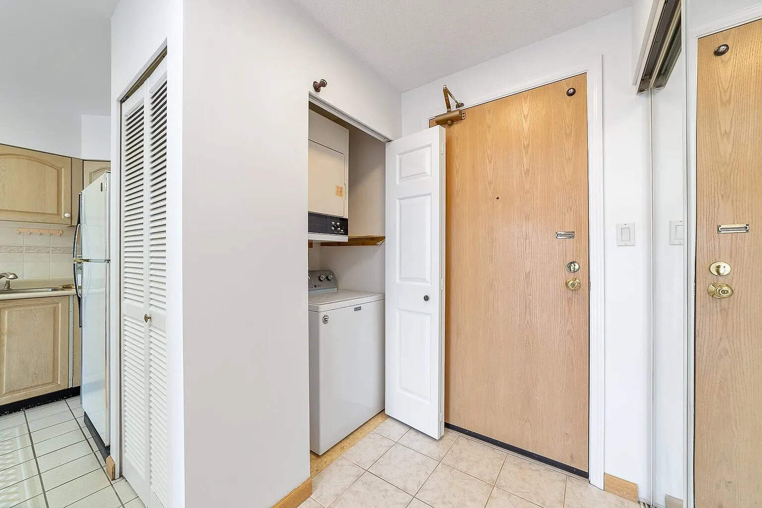 Bright laundry area with stackable washer and dryer, ample storage, and accessible entryway, part of a well-maintained home listed by Orca Realty Inc., ideal for real estate buyers and homeowners in BC.