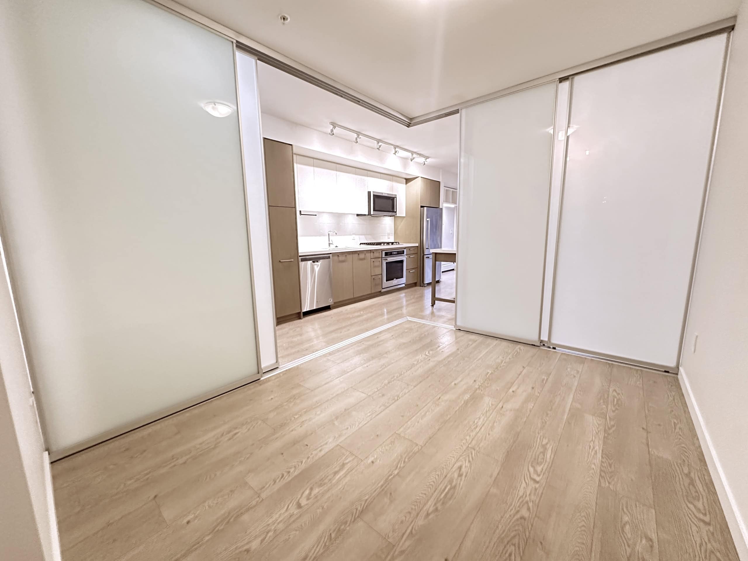 Bright modern kitchen with sliding frosted glass doors, hardwood flooring, stainless steel appliances, ideal for Vancouver real estate and property listings.