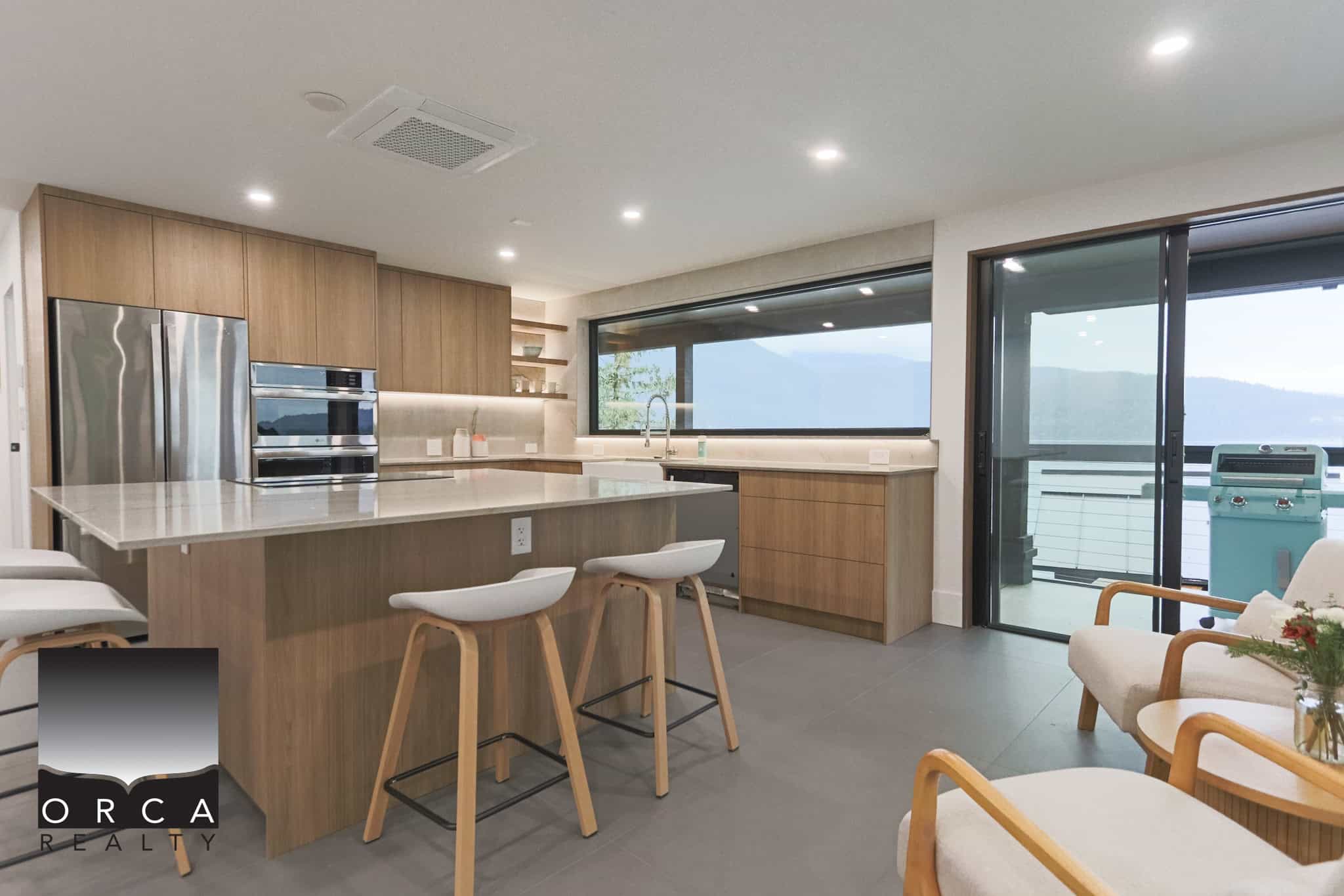Contemporary open-concept kitchen with modern cabinetry, stainless steel appliances, large windows, and a balcony with mountain views, perfect for Vancouver real estate and luxury homes.