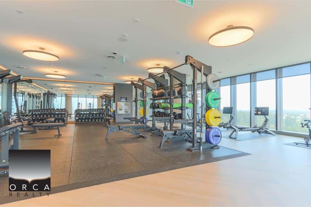 Modern gym interior at Orca Realty Inc. featuring advanced fitness equipment, free weights, and panoramic city views, ideal for healthy living and lifestyle in prime commercial real estate locations in Victoria.