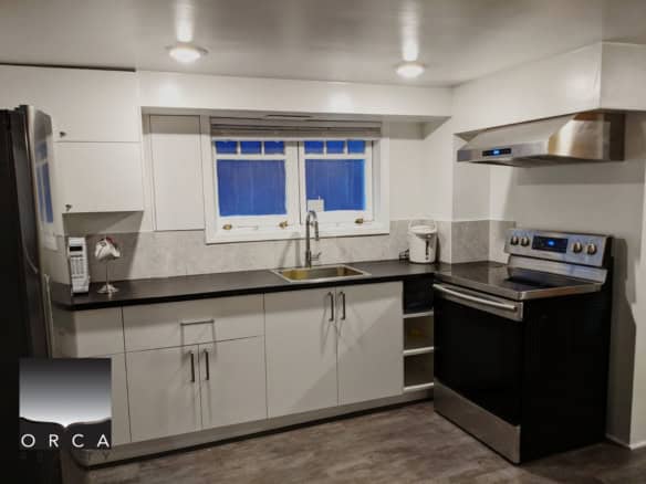 Modern kitchen with white cabinets, black countertop, stainless steel appliances, and a small window, perfect for Vancouver area real estate listings.