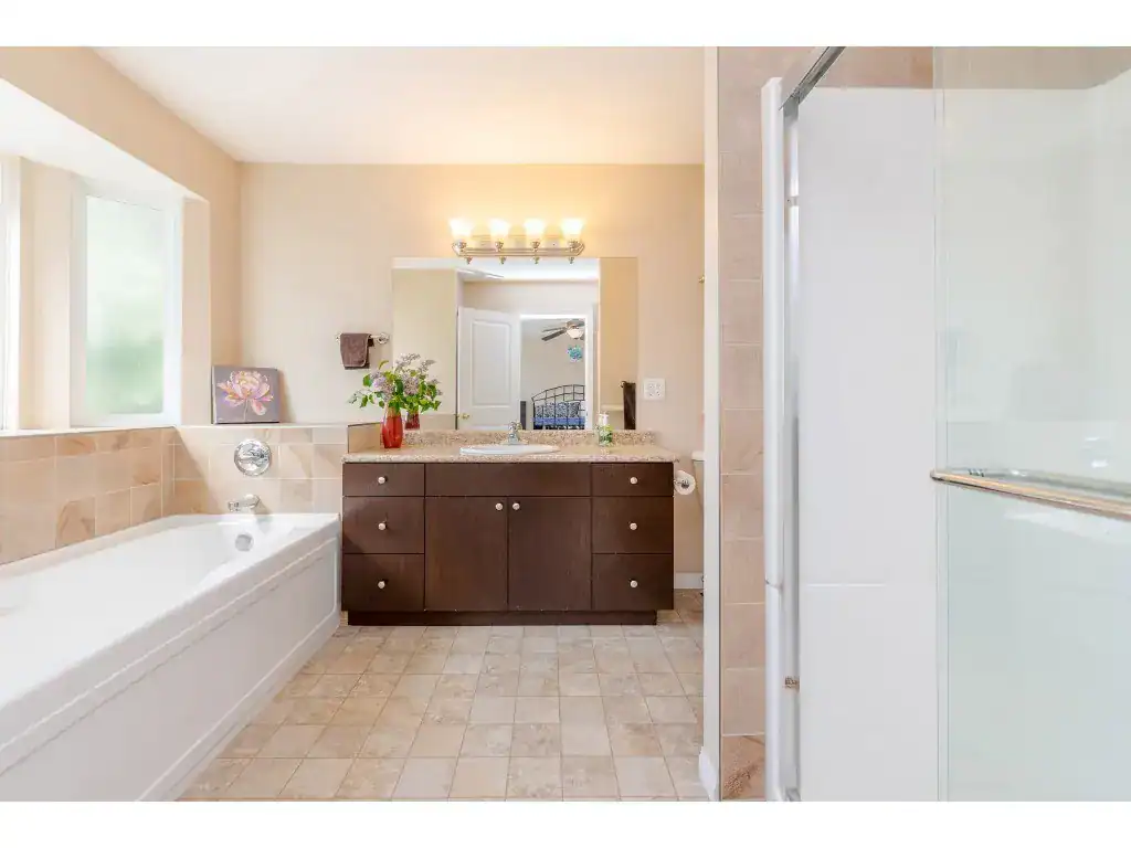 Bright bathroom with a bathtub, modern vanity with mirror, and walk-in shower, featuring natural light, beige tiles, and contemporary fixtures for comfort and style.