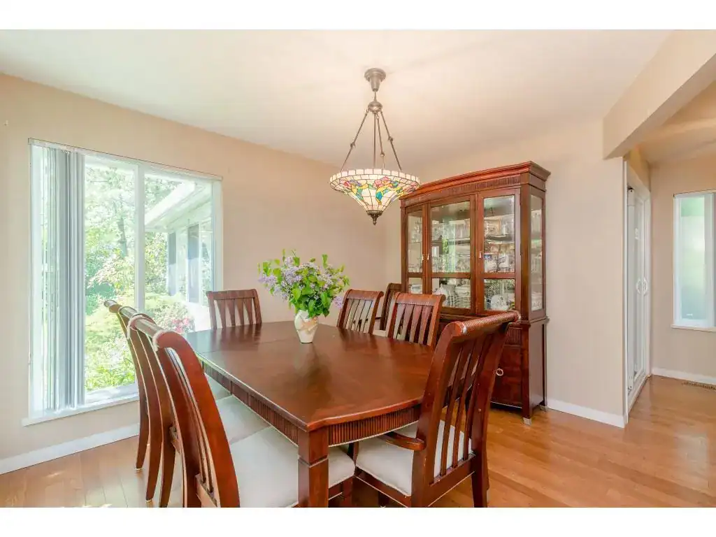 Spacious dining room with wooden furniture, elegant chandelier, and large windows offering natural light and garden views, ideal for family gatherings and entertaining guests in BC home.