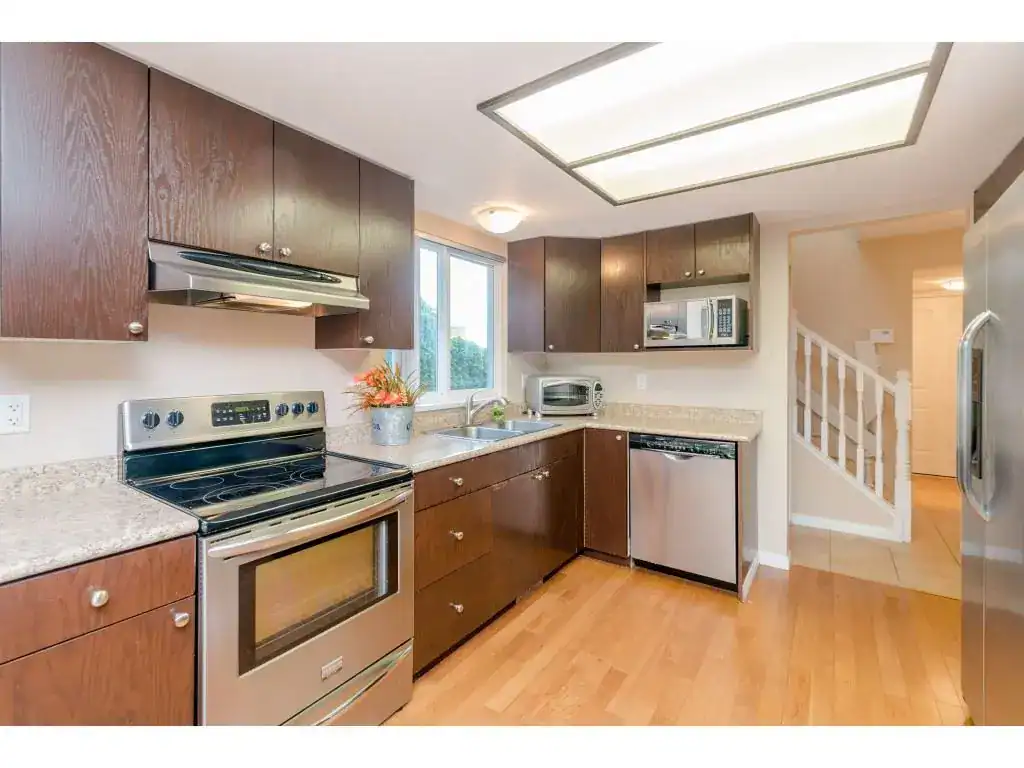 Modern kitchen with stainless steel appliances, wooden cabinetry, granite countertops, and natural light, ideal for Vancouver real estate market.