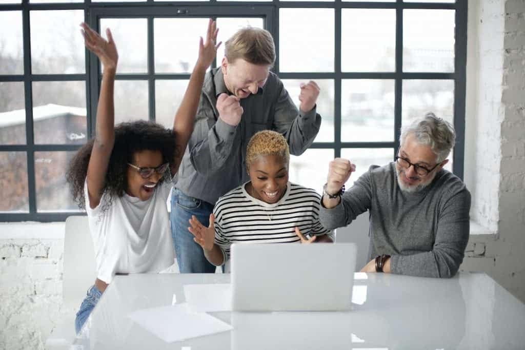 Excited diverse team celebrating success with laptop in modern office, representing Orca Realty Inc., expert in Vancouver real estate, property management, and home buying services.