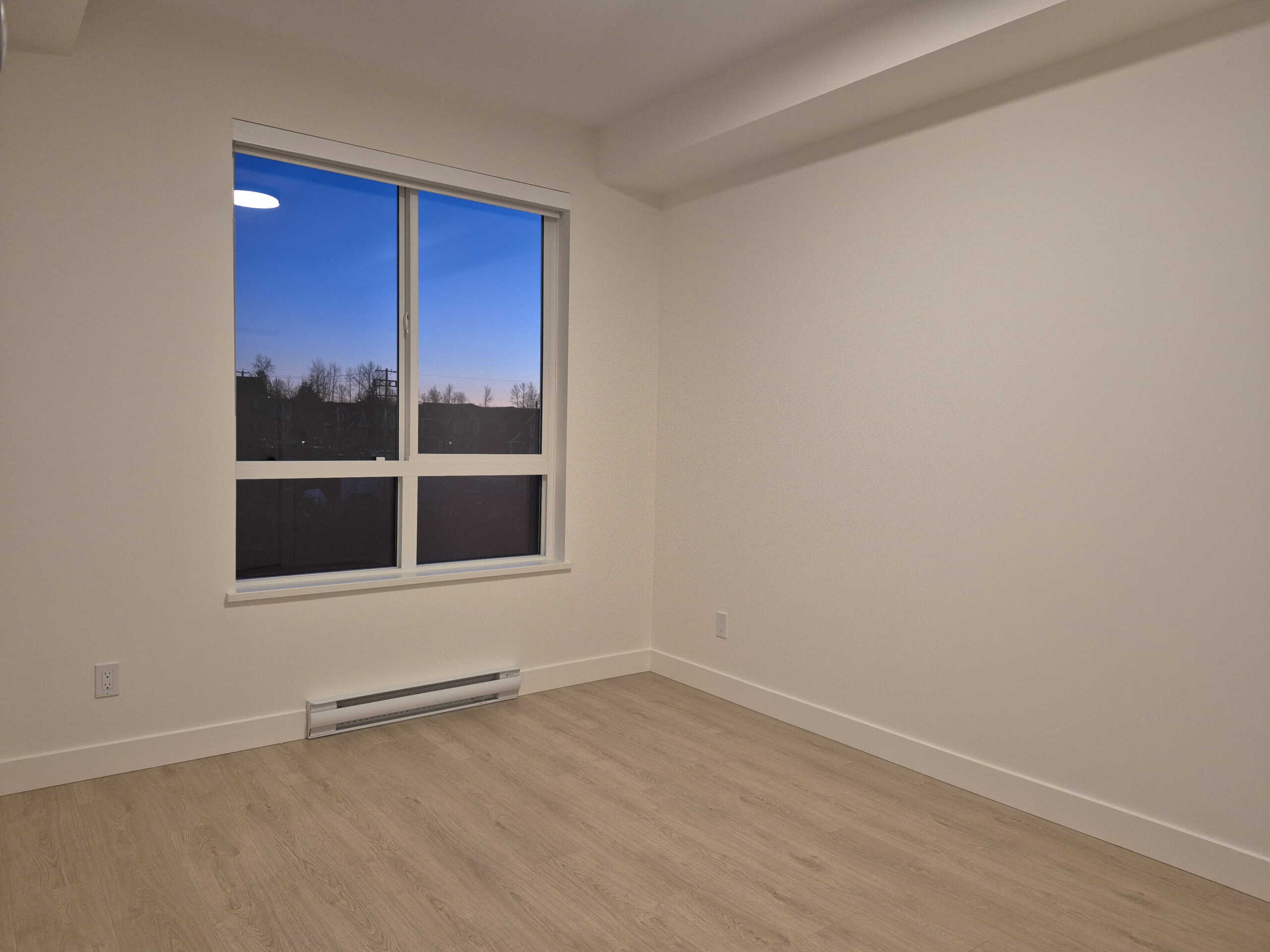 Bright empty room with large window showcasing a serene outdoor view, perfect for real estate listing photos or home staging.