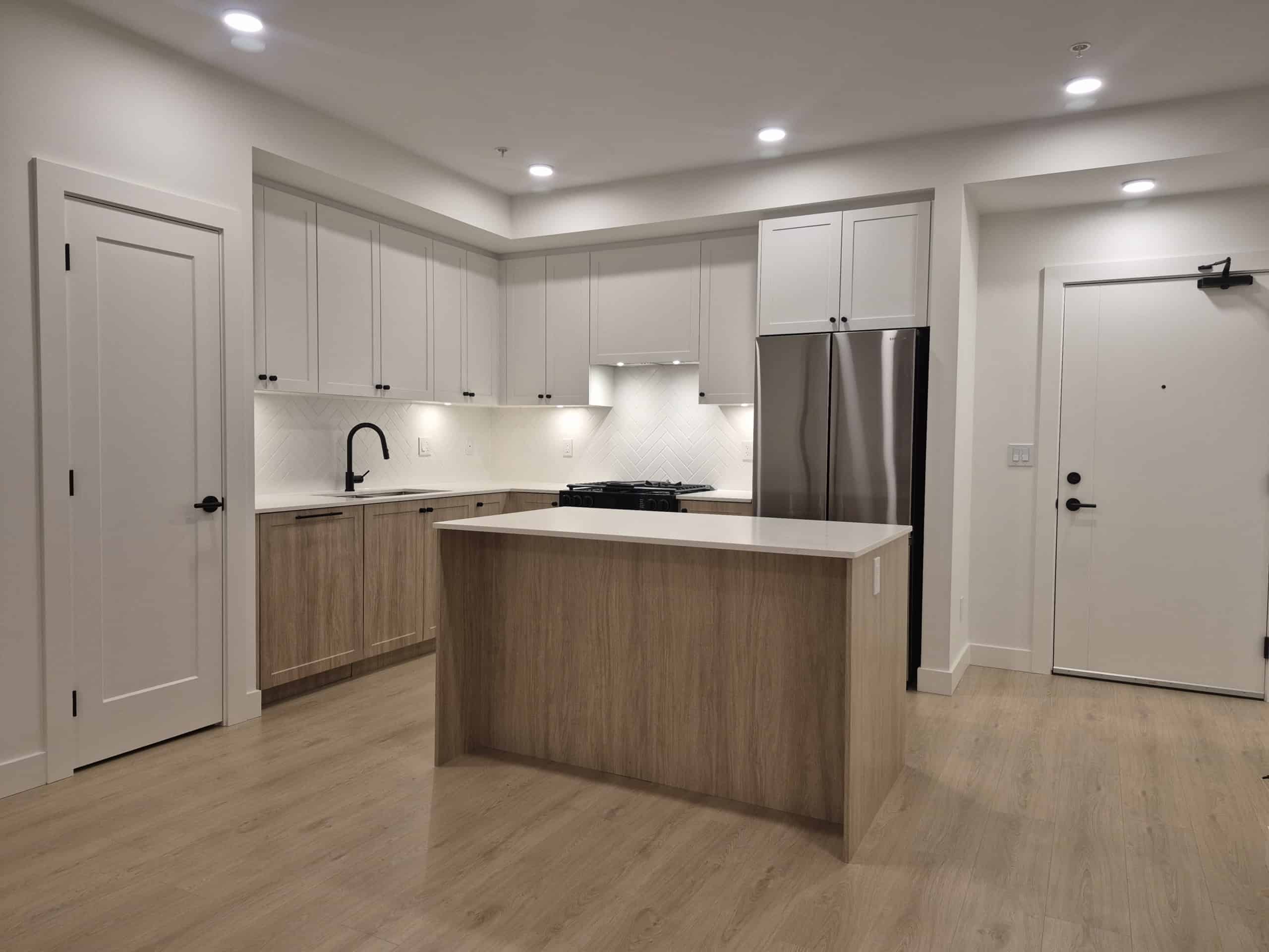 Modern kitchen with white cabinetry, stainless steel refrigerator, and natural wood accents, perfect for Vancouver Island real estate. Designed for stylish, functional living with high-quality appliances.
