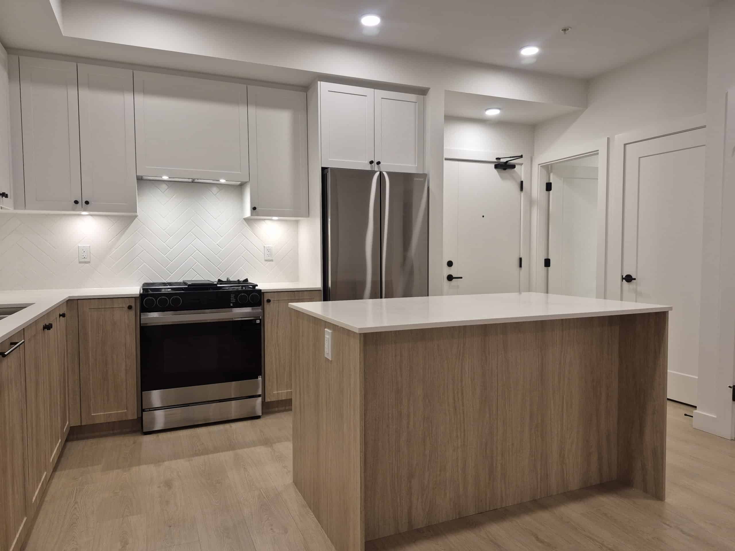 Bright modern kitchen with white and wood cabinets, stainless steel appliances, and a spacious island, perfect for homebuyers seeking contemporary residential real estate in Canada.