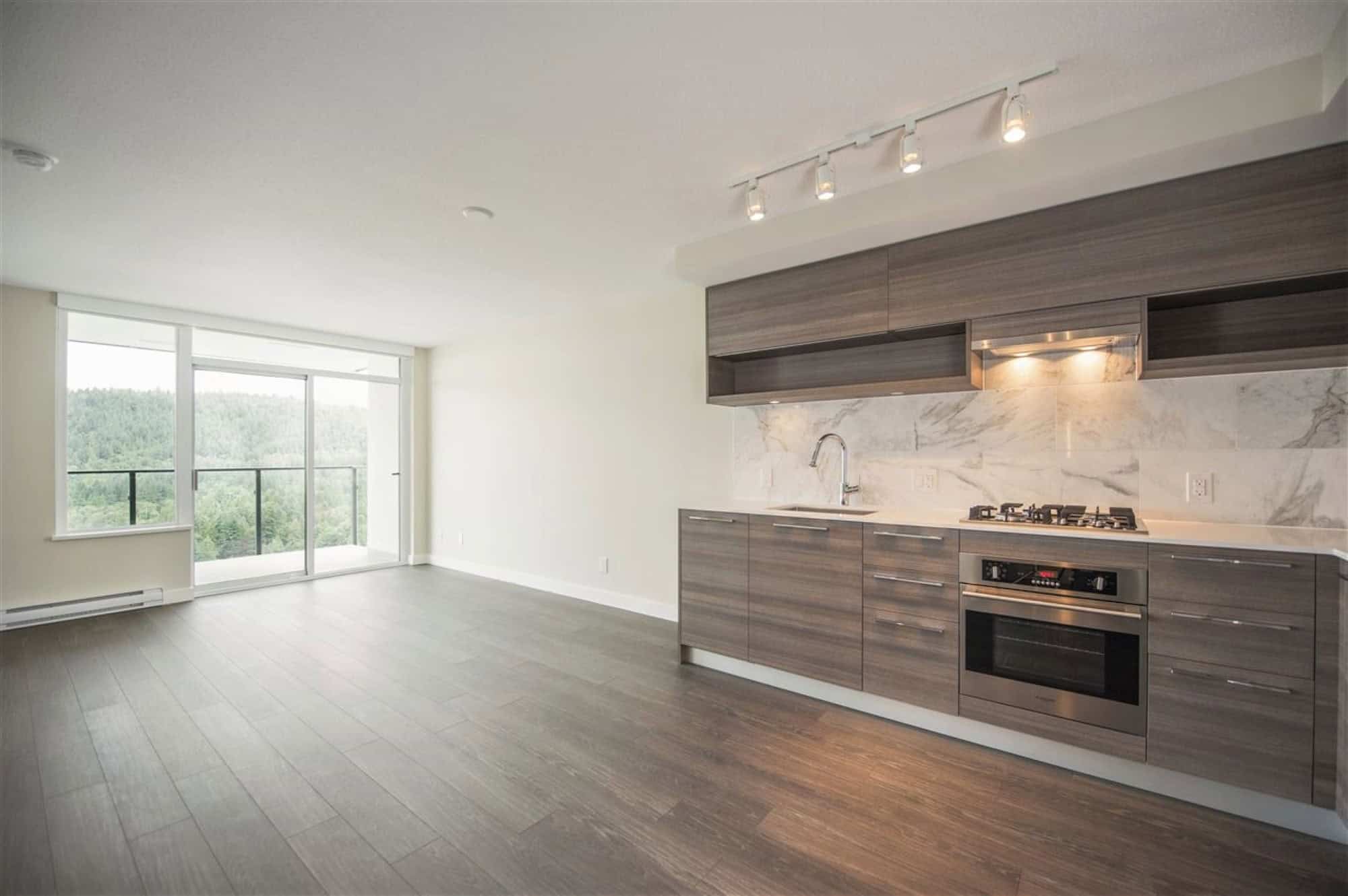 Spacious modern apartment living room featuring large windows, elegant kitchen with marble backsplash, and beautiful city views. Ideal for Vancouver real estate and investment opportunities.