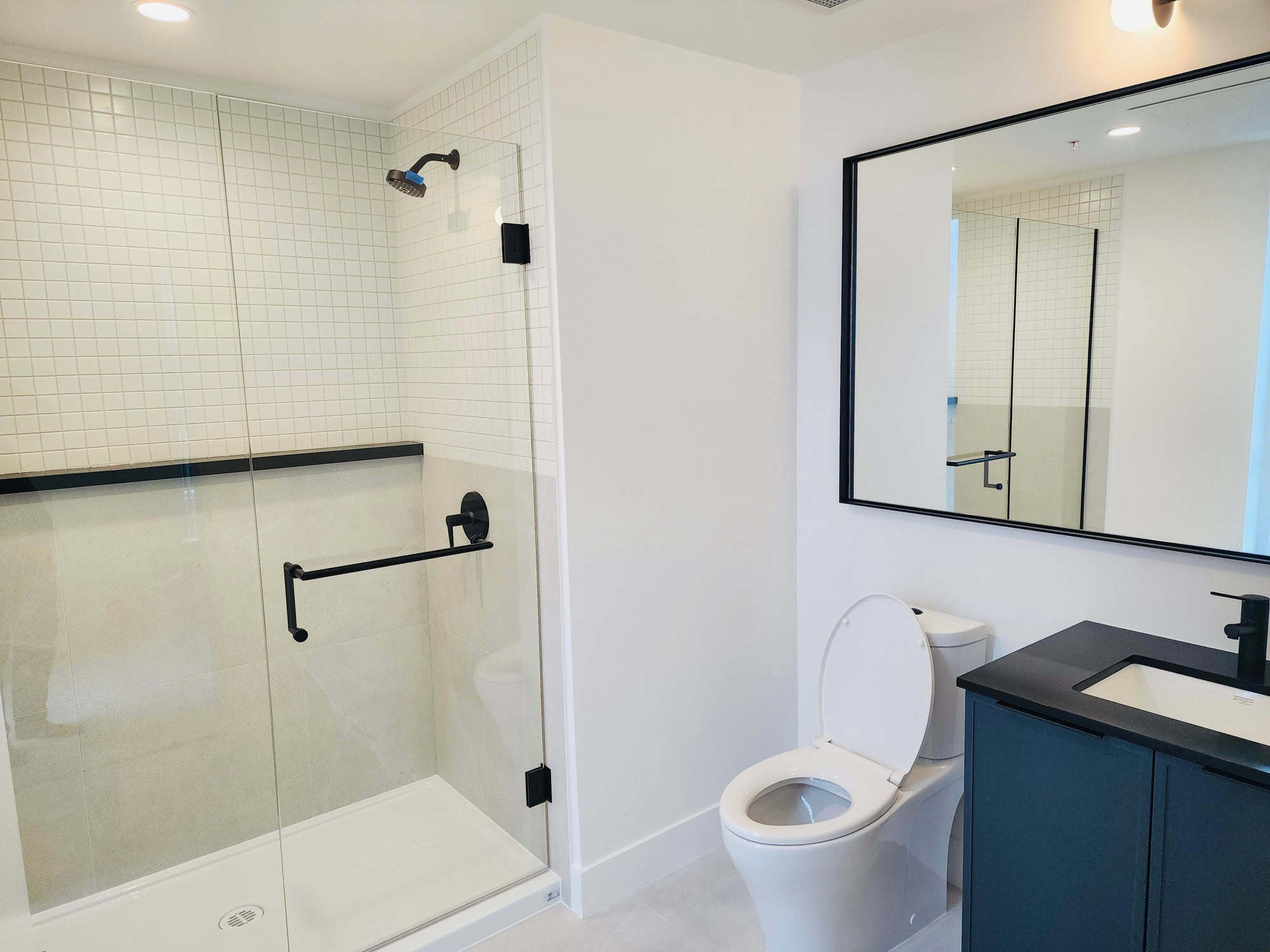 Modern minimalist bathroom with walk-in shower, white tile accents, black fixtures, and contemporary vanity with a large mirror for stylish and functional living space.