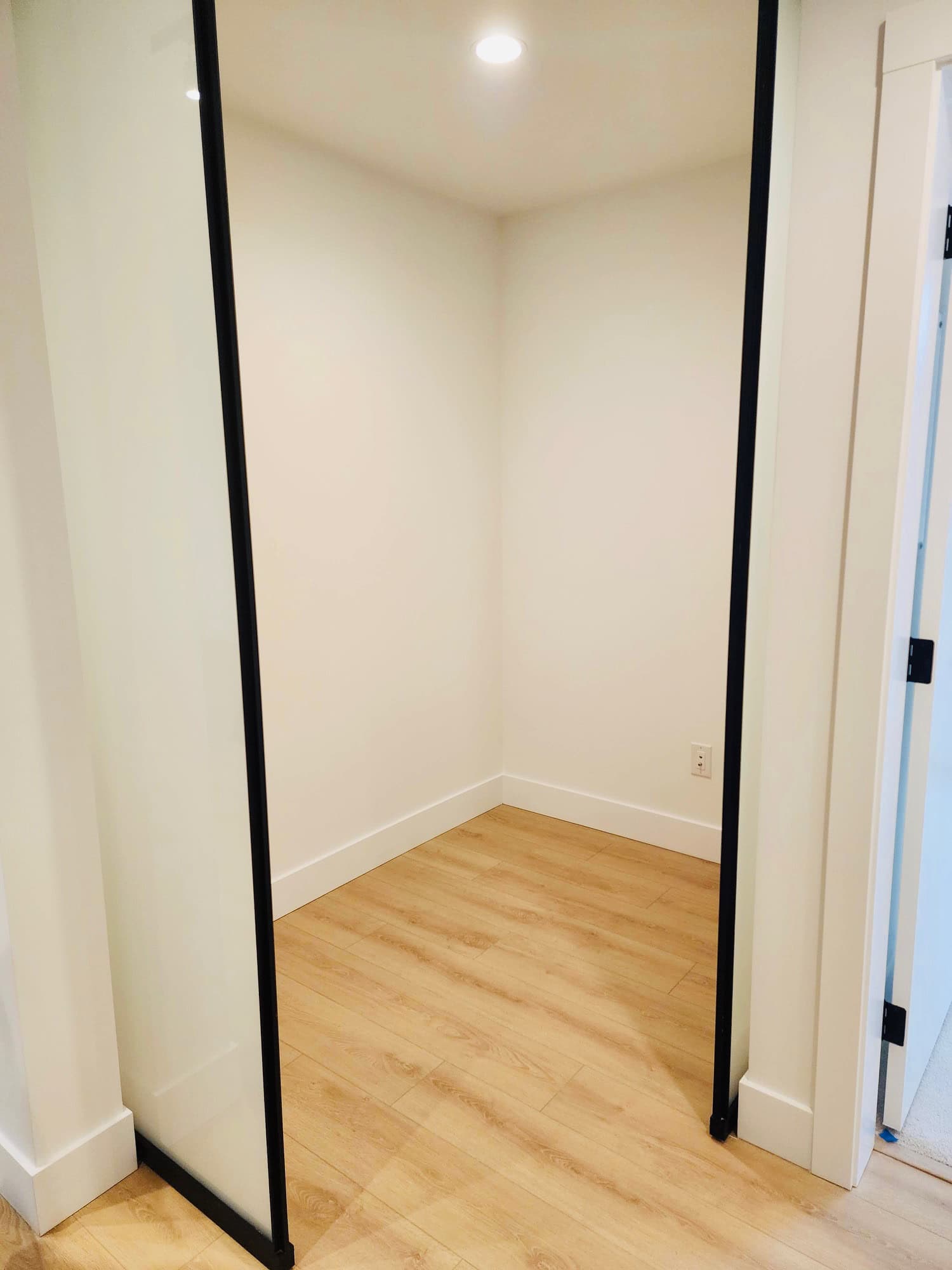 Bright empty walk-in closet with black-framed glass door, white walls, and wooden flooring, showcasing modern Vancouver real estate listings by Orca Realty Inc.