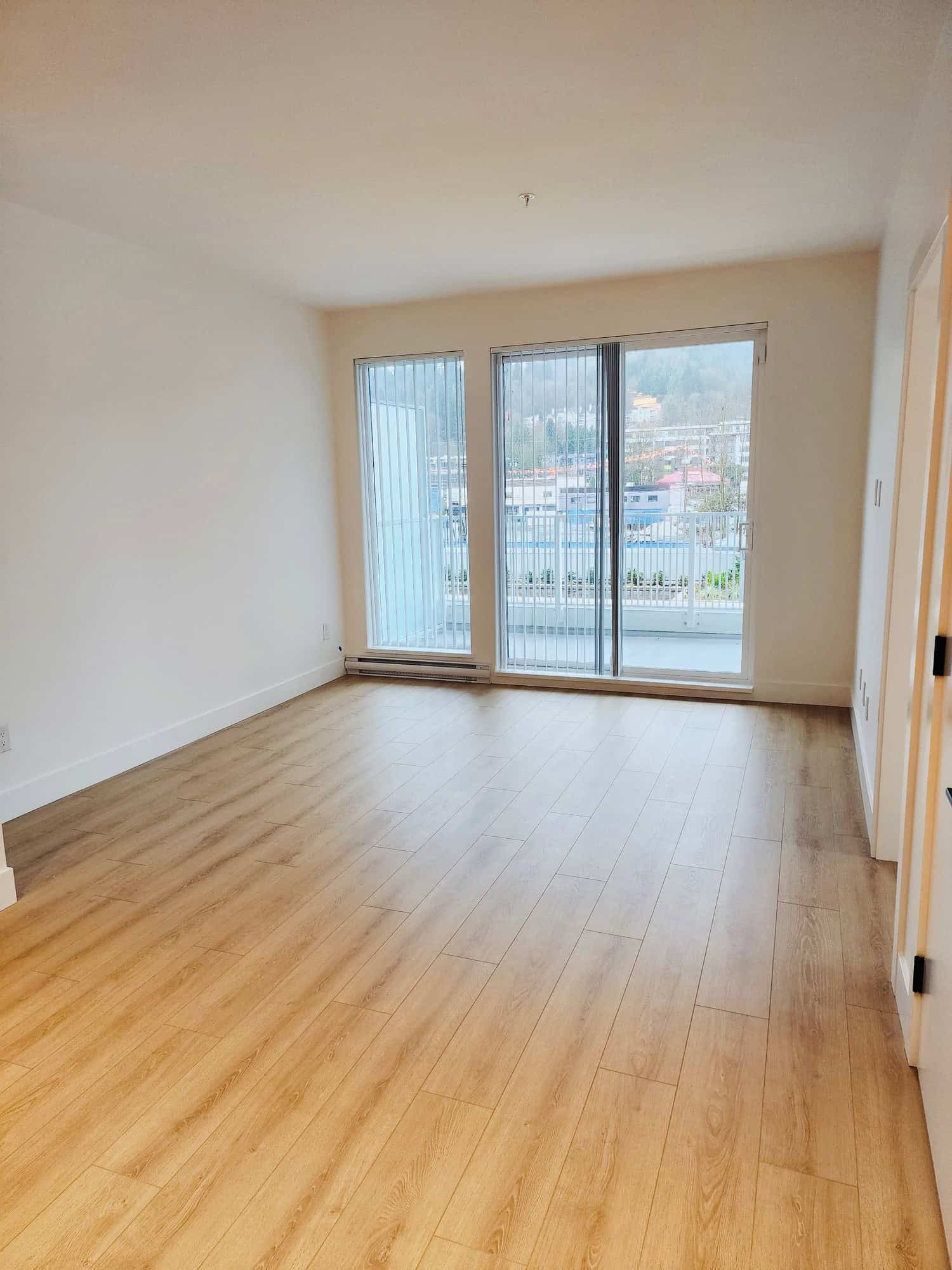 Bright living room with large glass sliding doors, balcony access, and natural light, perfect for Vancouver Island real estate. Hardwood floors and neutral walls enhance the space's appeal.