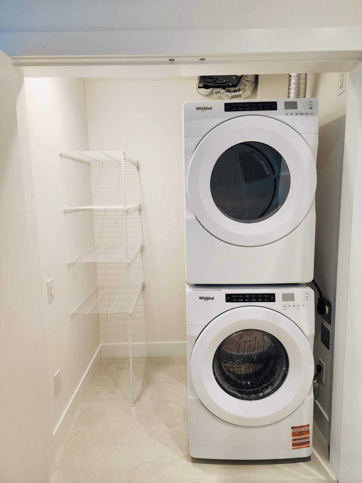 Modern laundry room with stacked Whirlpool washer and dryer, white wire shelving, fibre optic wall outlet, in-unit laundry amenities, ideal for property rental or home comfort.