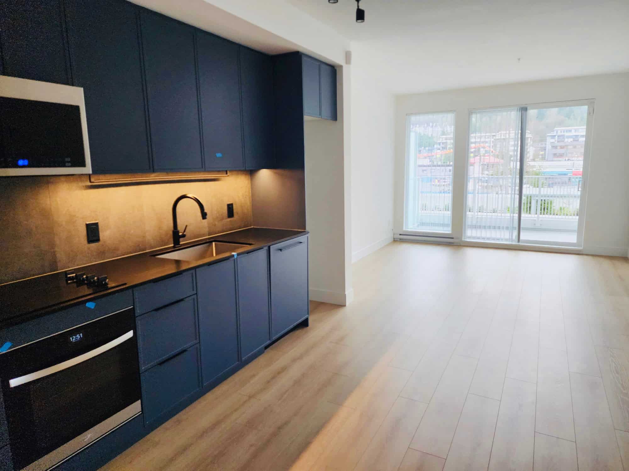 Bright modern apartment kitchen and living room with large windows, natural light, laminate flooring, and contemporary cabinetry, ideal for Vancouver real estate and property investment in BC.