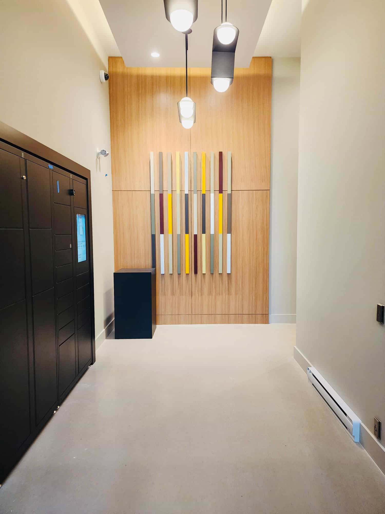 Modern residential lobby with stylish lighting, decorative wood panel wall art, and secure parcel lockers, showcasing high-quality condo amenities in Vancouver.