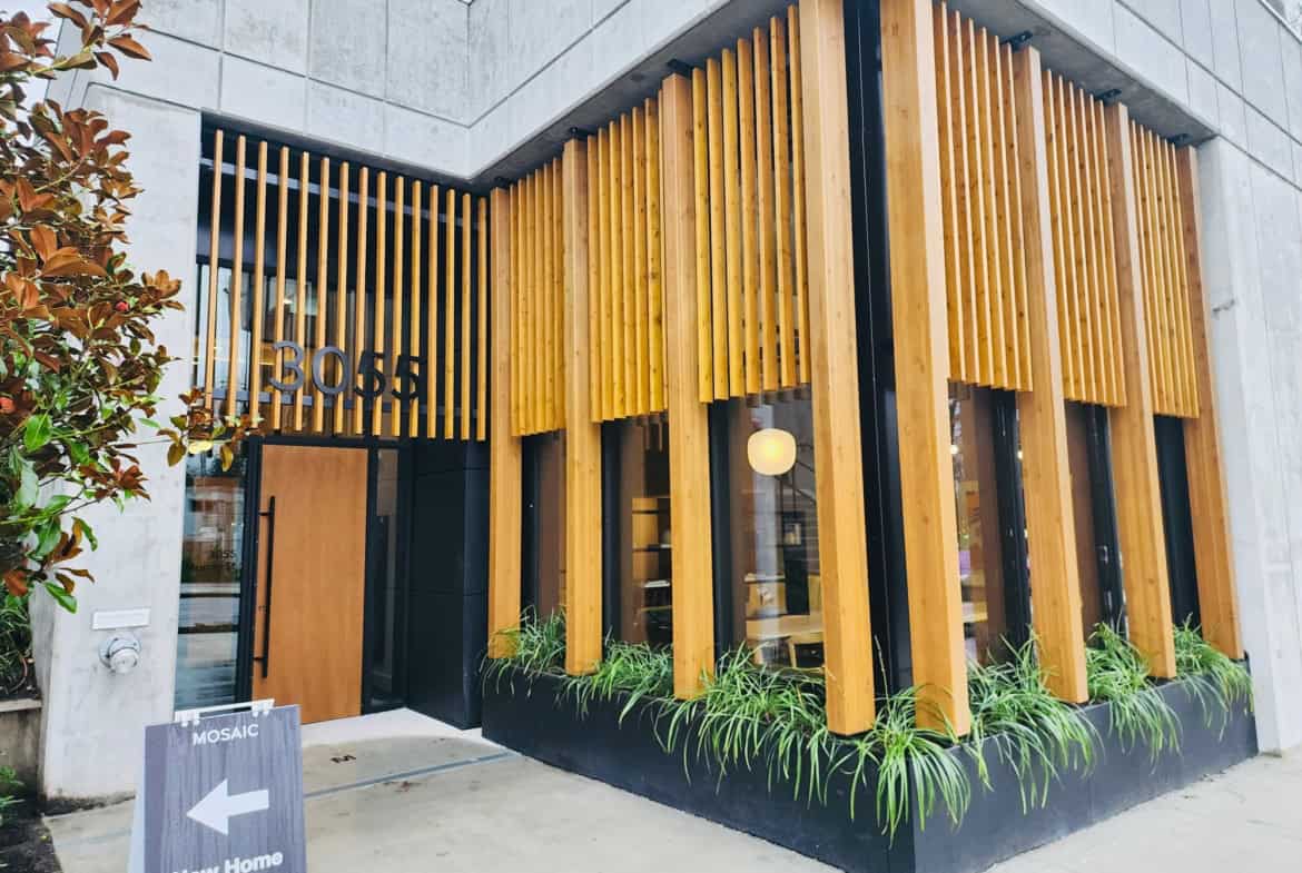 Stylish modern building entrance with wooden slats, black accents, and greenery, showcasing contemporary architecture and prime real estate in Vancouver, BC.
