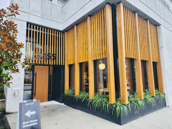 Stylish modern building entrance with wooden slats, black accents, and greenery, showcasing contemporary architecture and prime real estate in Vancouver, BC.