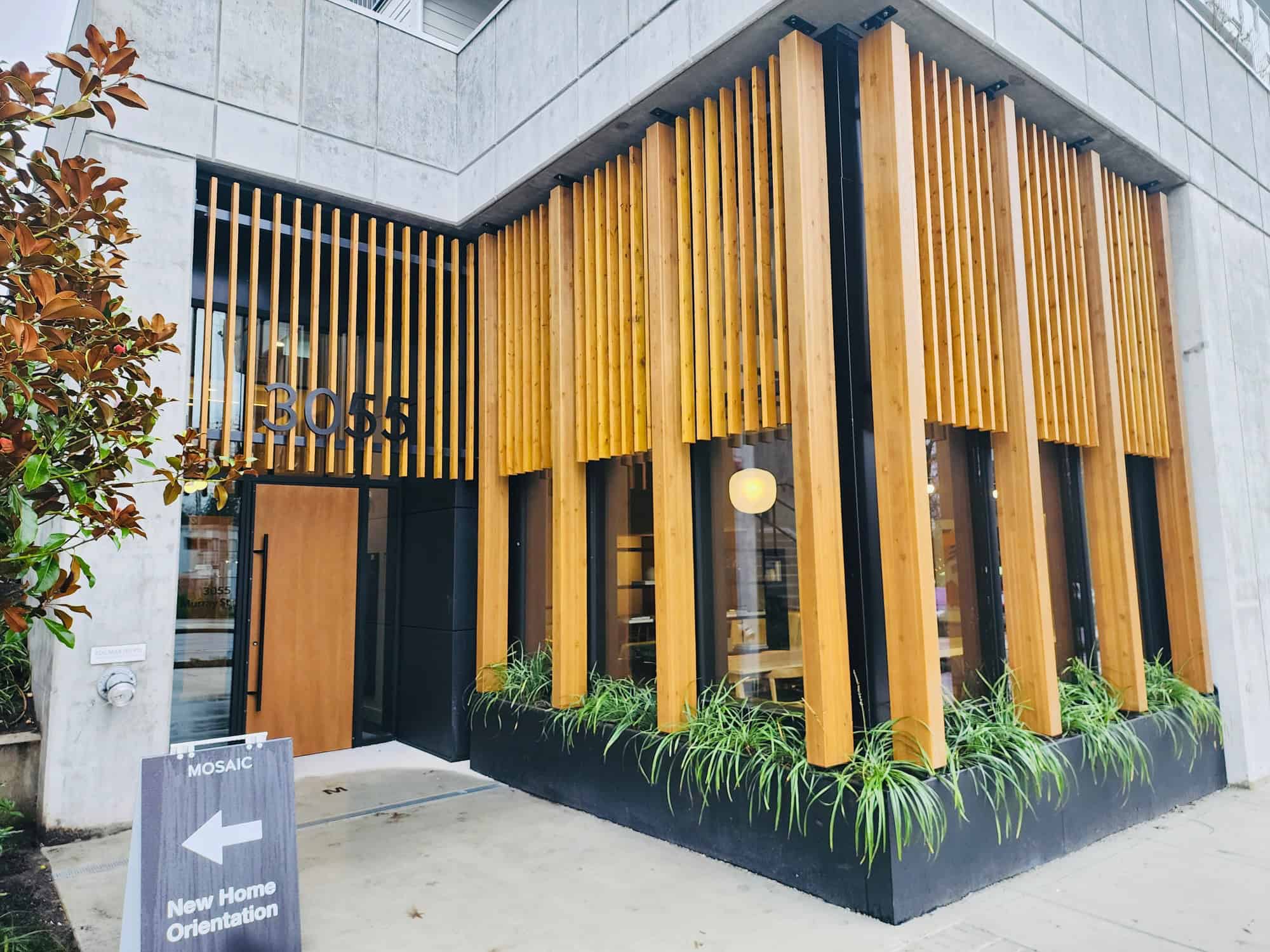Stylish modern building entrance with wooden slats, black accents, and greenery, showcasing contemporary architecture and prime real estate in Vancouver, BC.