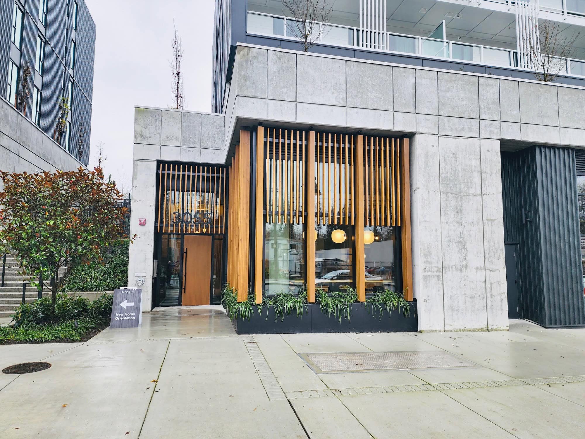 Modern condominium building entrance with contemporary architectural design, wooden accents, and well-maintained landscaping, reflecting Vancouver's vibrant real estate market.