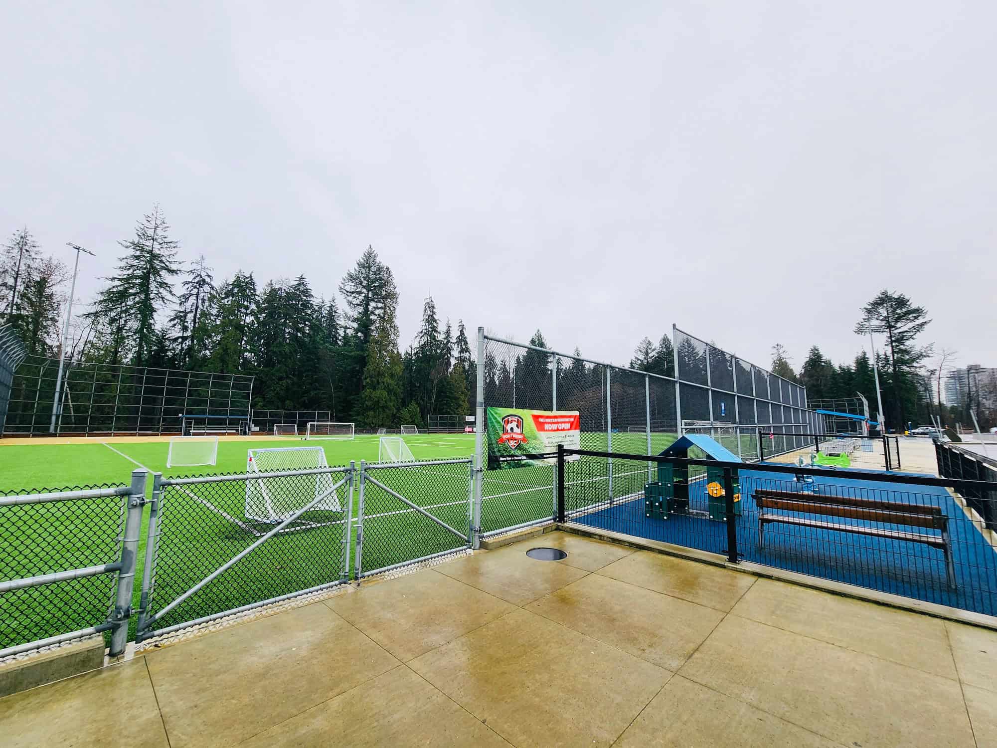 Bright outdoor sports field with green artificial turf, soccer goals, seating area, and surrounding tall trees, ideal for community recreation and sports activities in Vancouver.