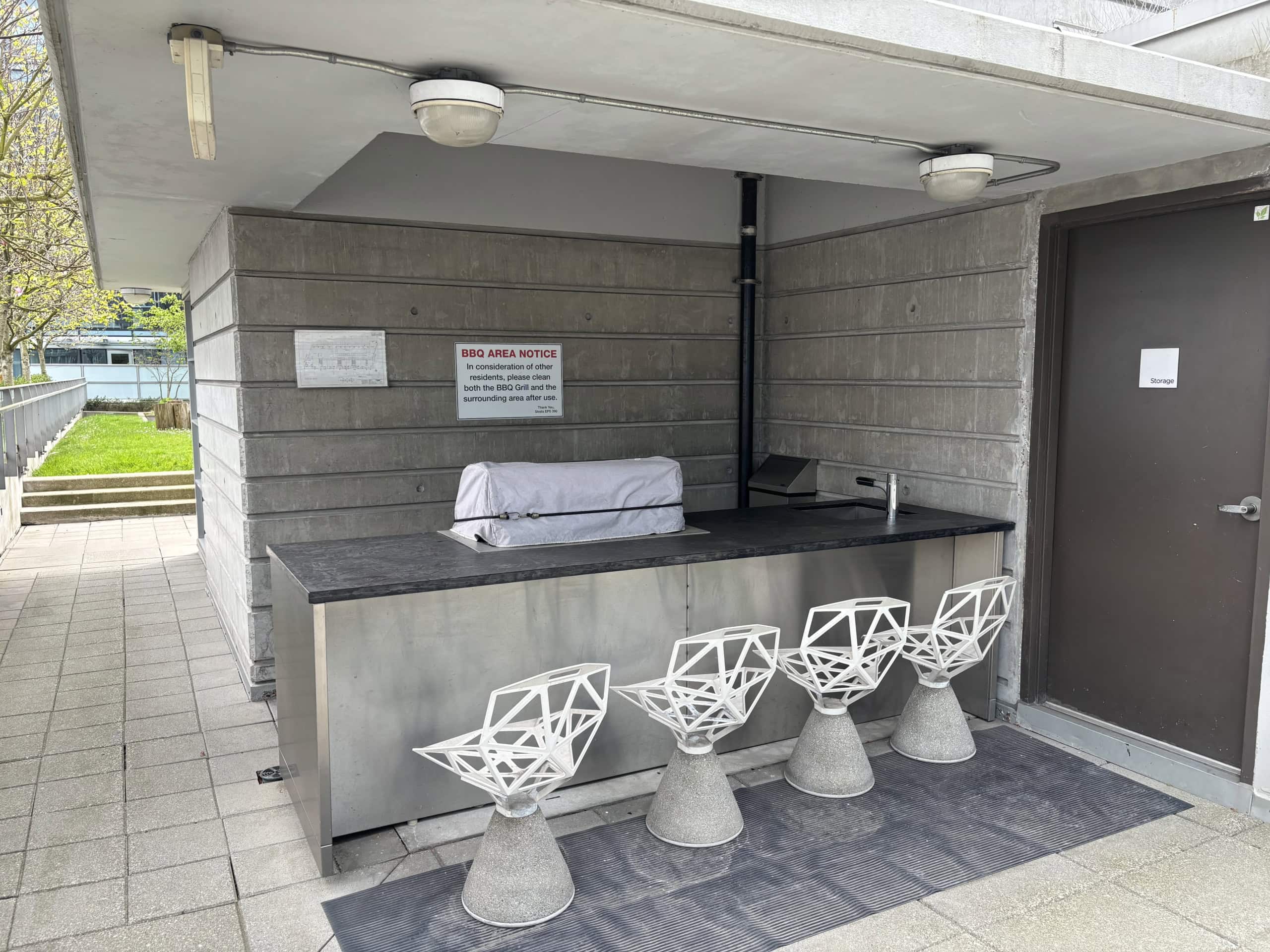 24 Modern outdoor BBQ area with seating for residents, featuring contemporary white chairs, a grill, and a nearby storage room, perfect for social gatherings at Orca Realty Inc.