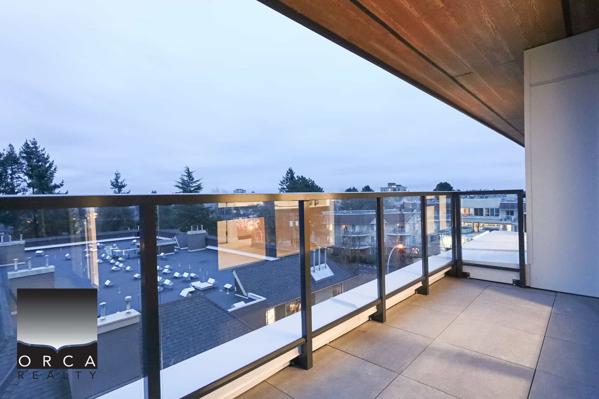Spacious modern balcony with glass railing overlooking Vancouver skyline and city rooftops, ideal for outdoor living, sunset views, and entertaining in a contemporary Orca Realty property in Vancouver, BC.
