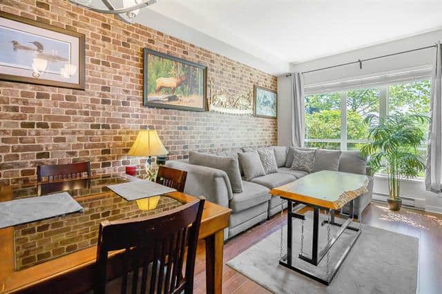 Bright living room with large windows, modern grey sofa, brick accent wall, and stylish decor, ideal for Vancouver real estate listings and showcasing downtown condos or house interiors.