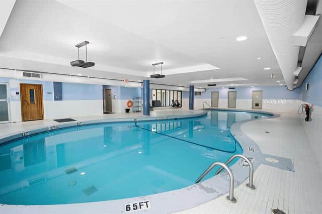 Indoor heated swimming pool at Orca Realty Inc. luxury property, featuring a modern design, clean white tiles, and accessible entry for residents in a premium real estate development.
