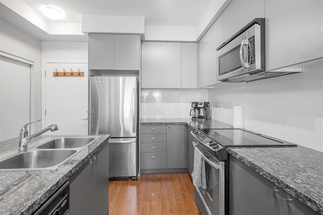 Modern kitchen with stainless steel appliances, granite countertops, grey cabinets, electric stove, microwave, and coffee maker in a contemporary condo.