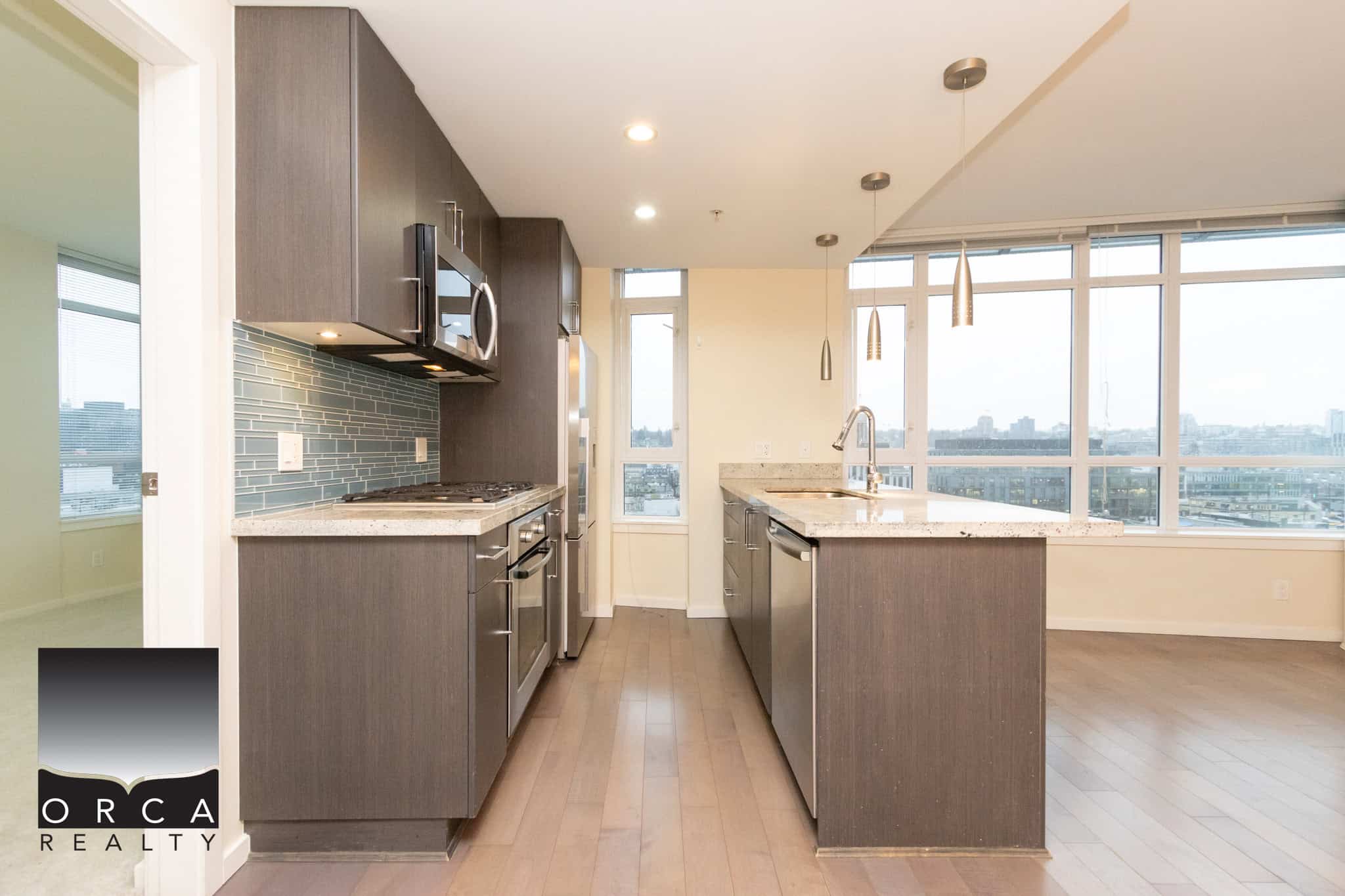 5 (4) Modern kitchen with dark cabinetry, granite countertops, stainless steel appliances, and large city-view windows in a high-rise condo. Perfect for urban living and entertaining.