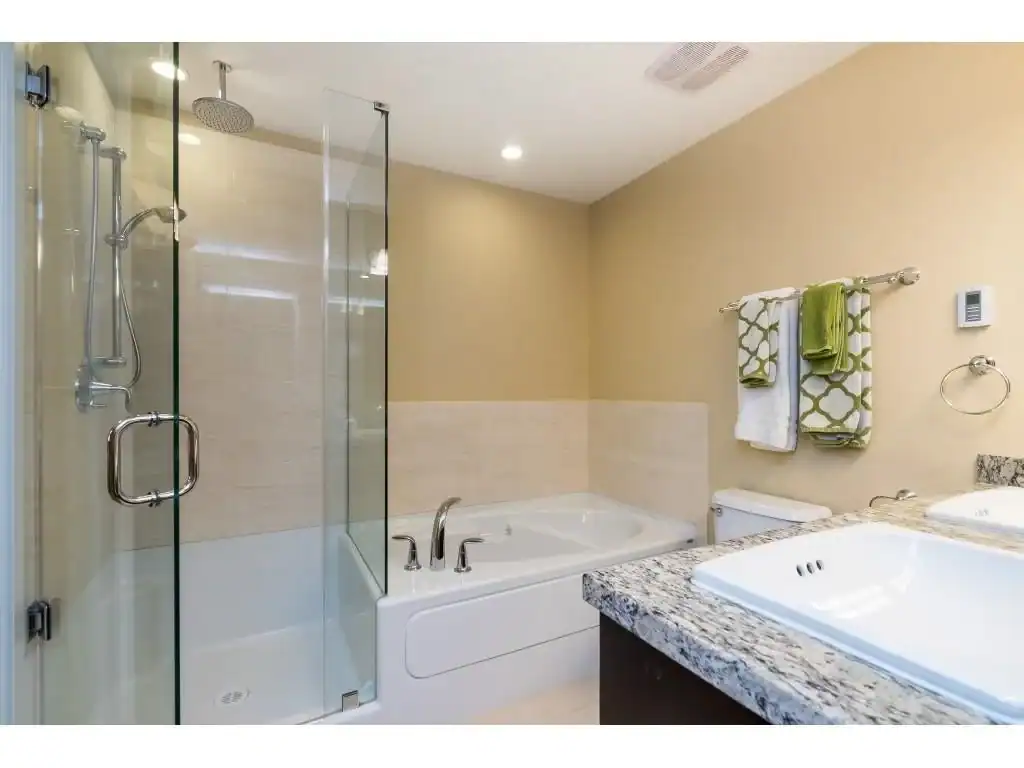 Modern bathroom with glass shower, soaking tub, granite countertop, and stylish towels, showcasing high-quality home features for buyers interested in Orca Realty Inc. properties.