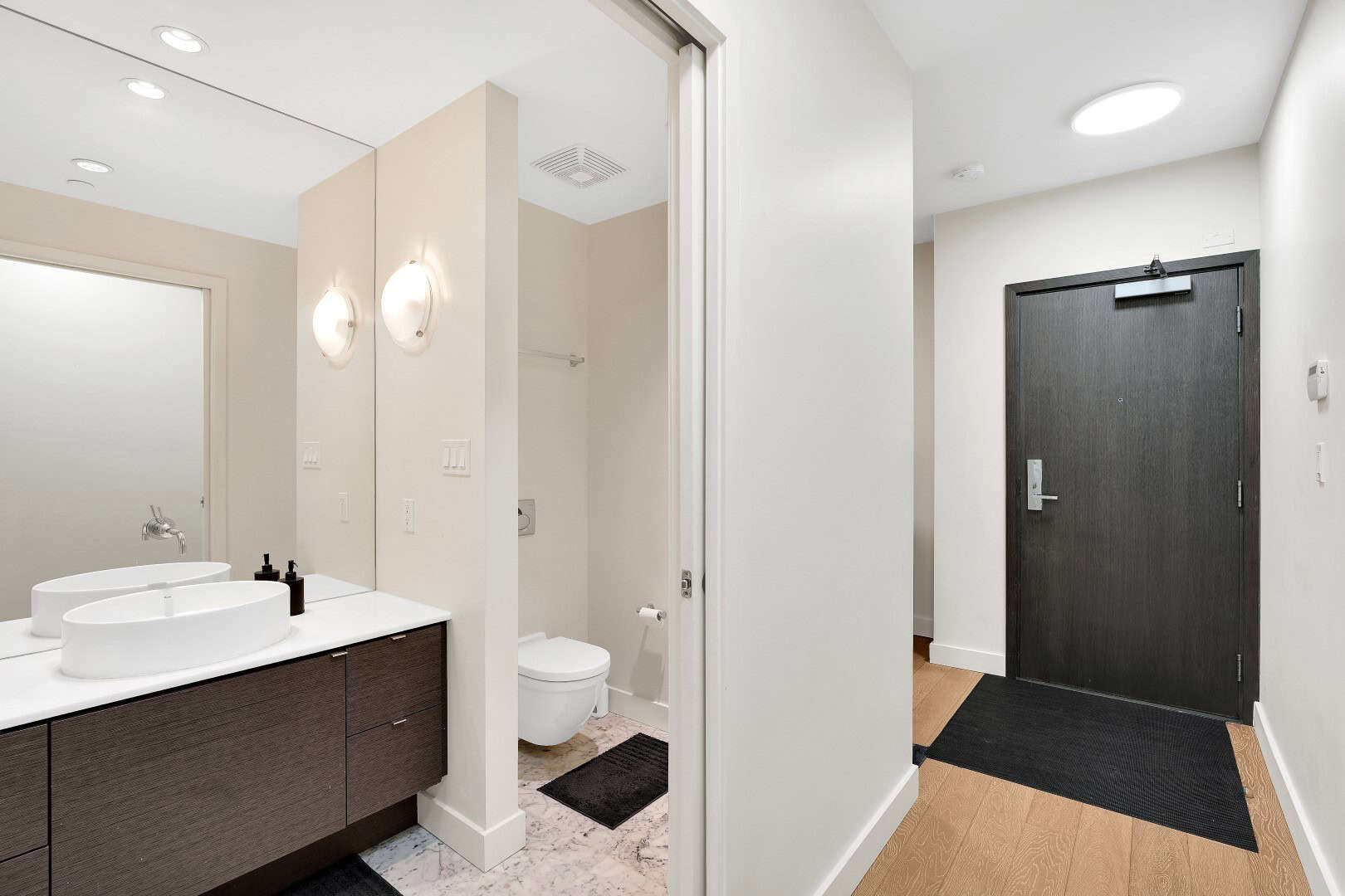 7 Bright modern Vancouver home bathroom featuring sleek vanity with vessel sinks, toilet area, and stylish wooden door, showcasing contemporary interior design with neutral tones and efficient space utilization.