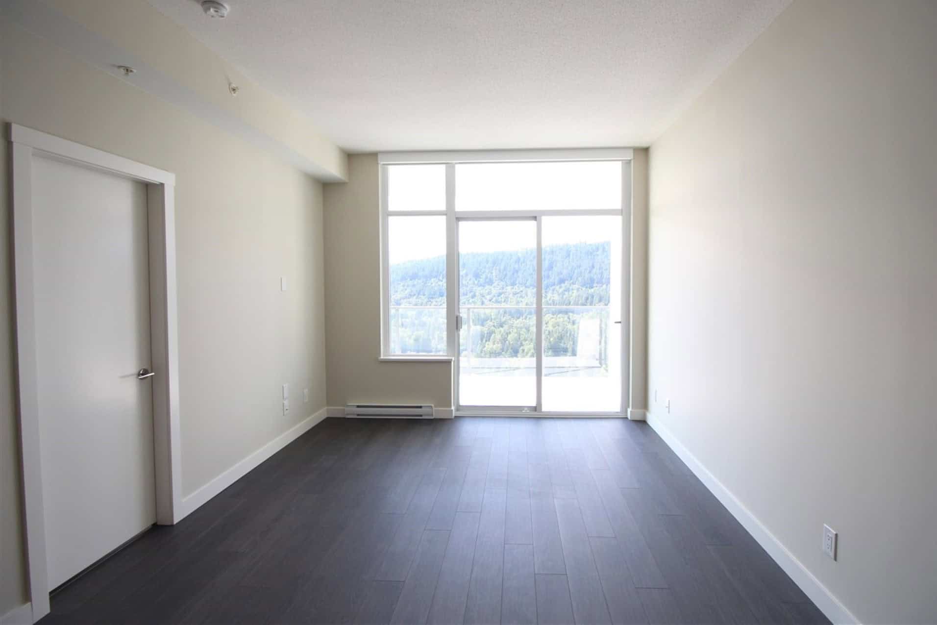Bright modern apartment living room with large window overlooking scenic mountain view, featuring neutral walls and dark laminate flooring, perfect for Vancouver real estate or BC property buyers.