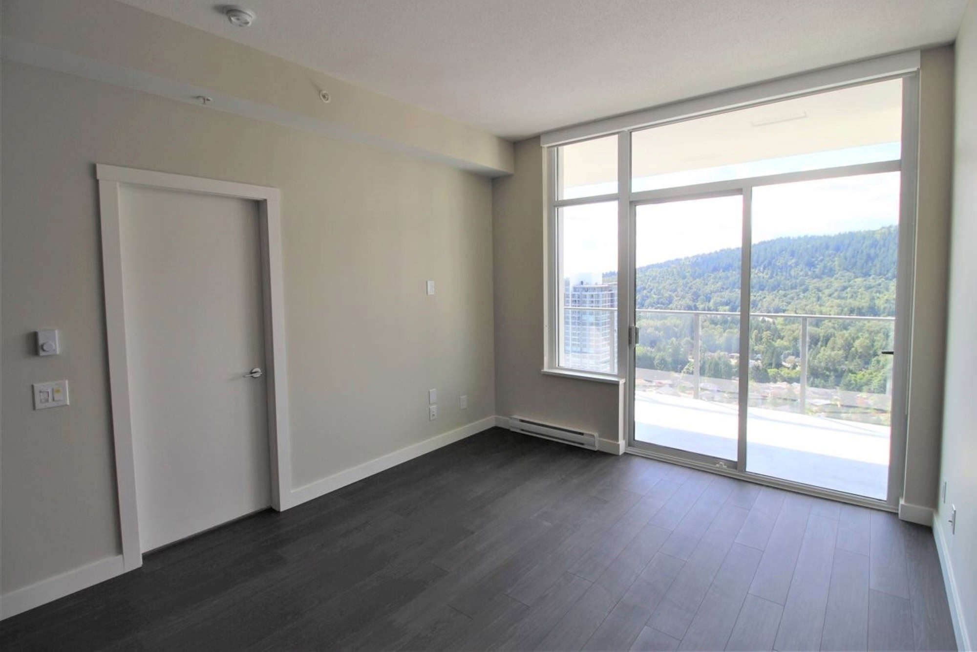 Bright modern apartment interior with large glass balcony door showcasing scenic mountain views in Vancouver, Canada – perfect for urban living with natural light.