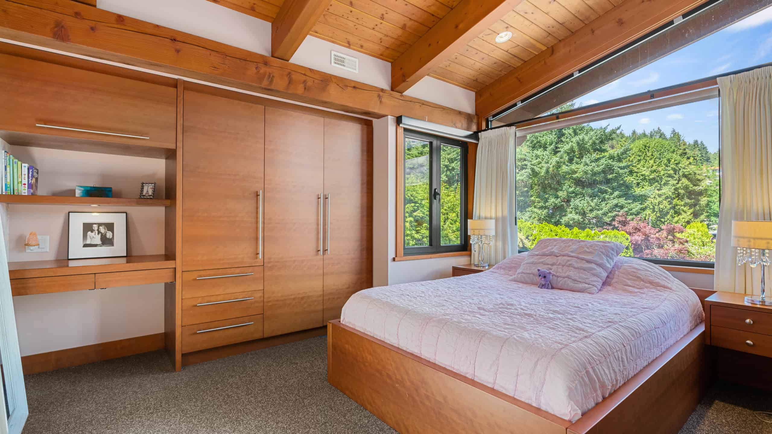 Cozy Bedroom with Scenic Views An inviting bedroom featuring a large window overlooking lush greenery, wooden accents, and natural light, perfect for relaxing in West Vancouver.
