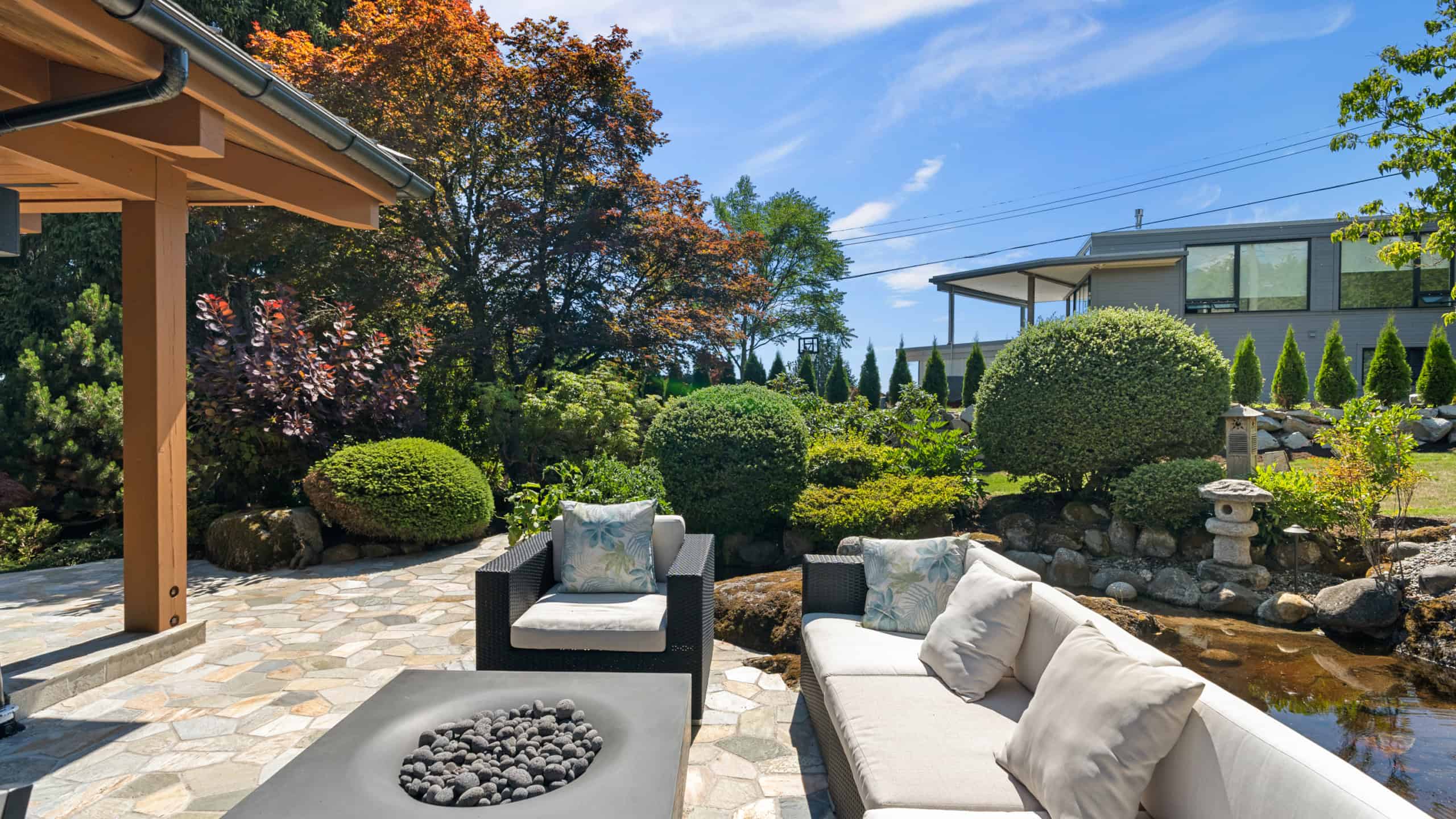Elegant West Vancouver Garden Scene with Seating Area and Water Feature Beautiful outdoor living space in West Vancouver featuring modern seating, lush landscaping, and a tranquil water feature under a clear blue sky.