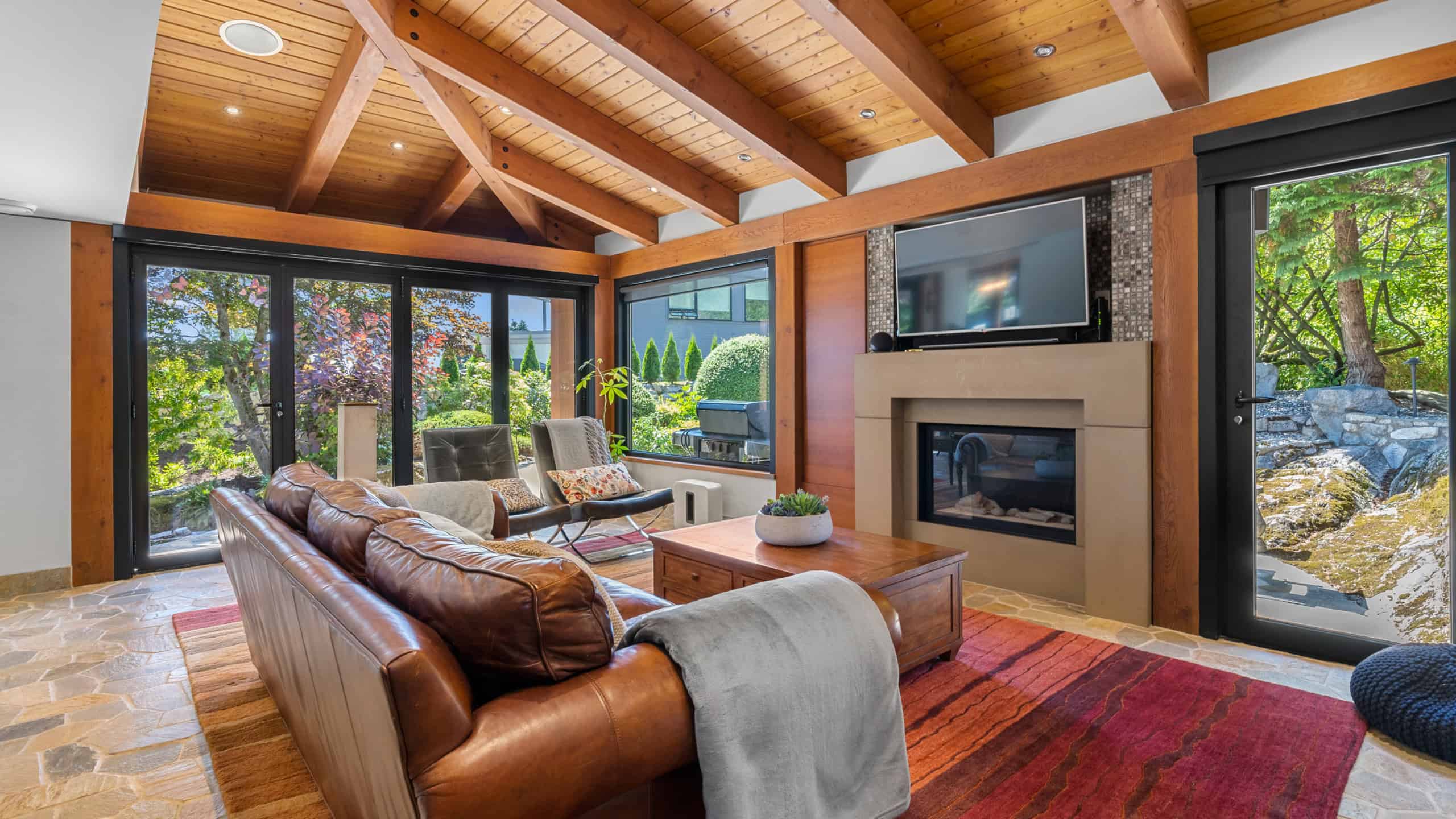 Modern Living Room with Natural Light and Scenic Views Bright and spacious living room featuring large windows with views of lush greenery, a cozy fireplace, and stylish furniture, perfect for relaxing or entertaining in West Vancouver.