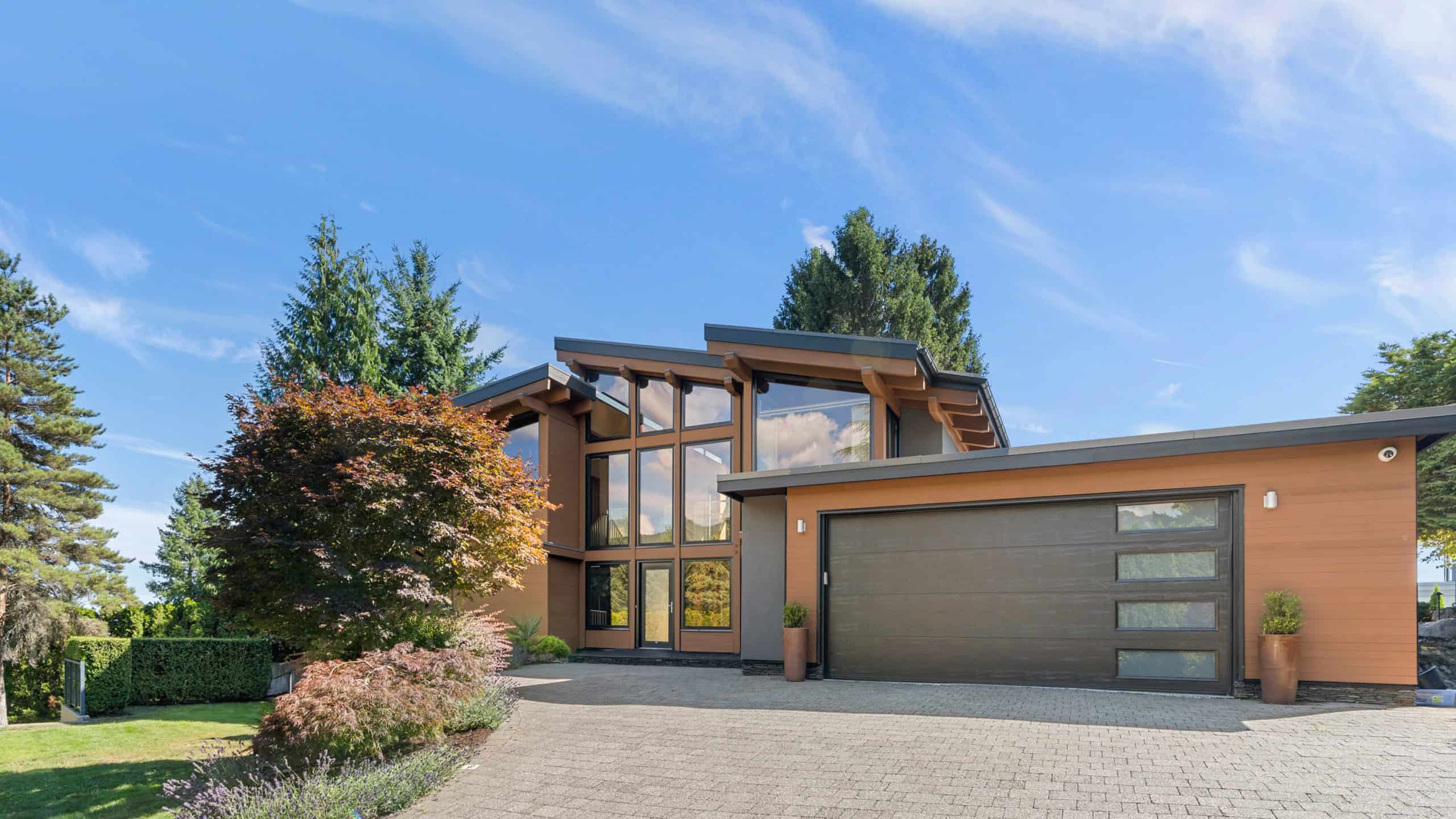 Modern West Vancouver Home Exterior Contemporary West Vancouver residence with large glass windows, lush landscaping, and a spacious driveway, showcasing luxury real estate in the area.