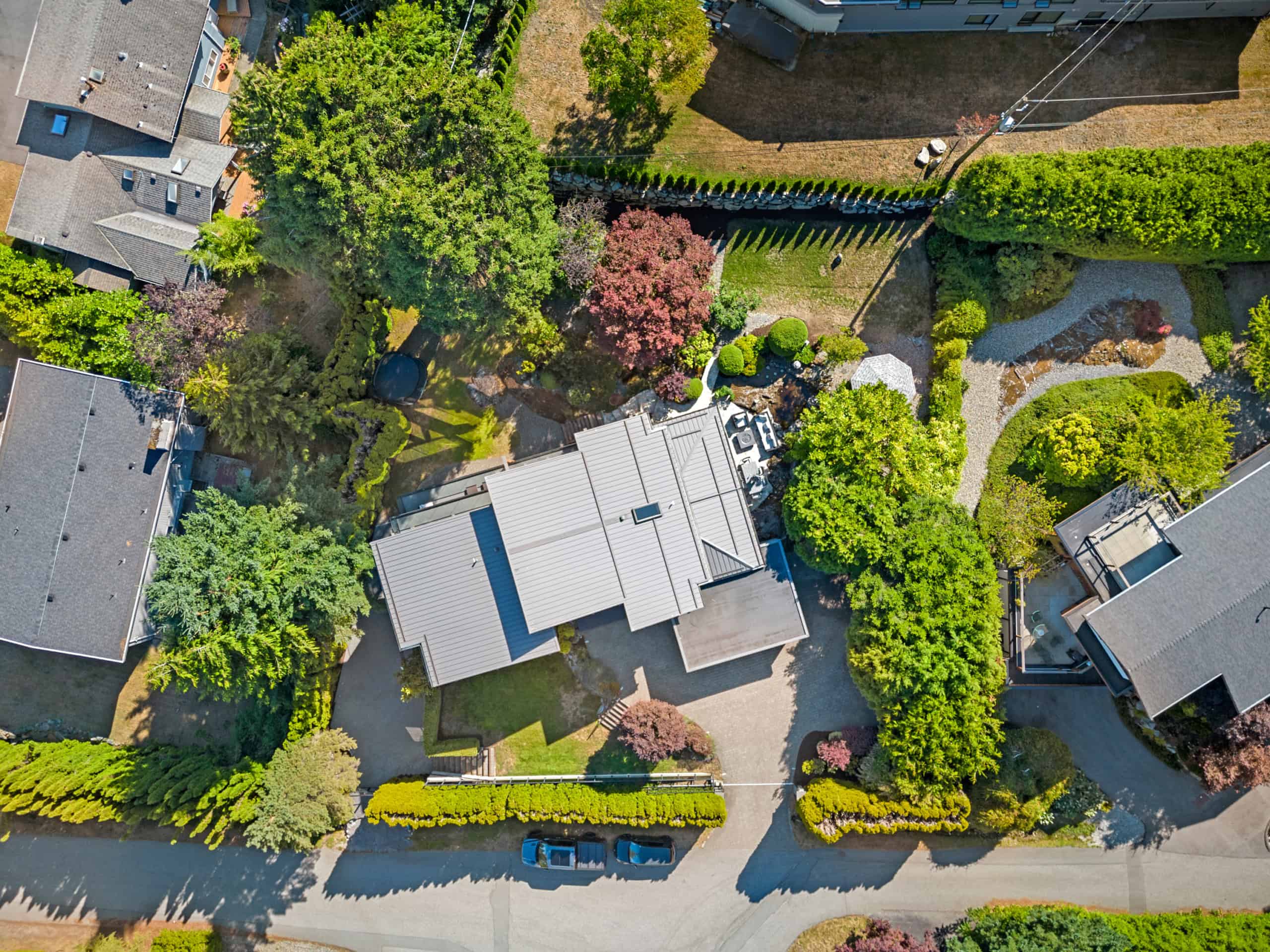 Modern West Vancouver Home with Lush Garden Aerial view of a contemporary West Vancouver residence surrounded by mature trees and landscaped gardens, showcasing a spacious backyard and driveway.