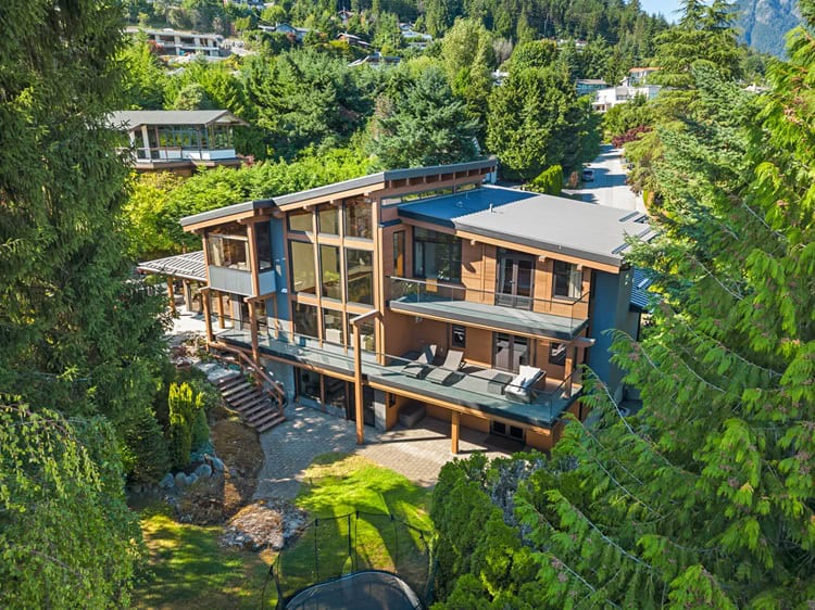 Elegant contemporary house in West Vancouver surrounded by lush greenery and tall trees. Features large windows, spacious decks, and a stylish exterior blending with natural landscape.