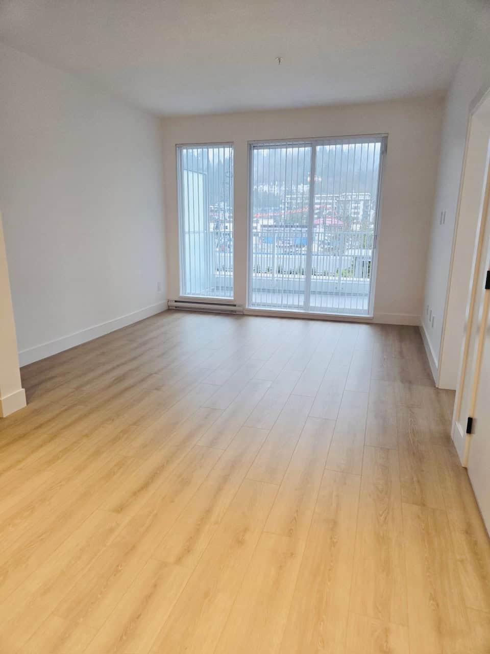 Bright modern living room with large floor-to-ceiling windows, white walls, and light wood flooring, ideal for Vancouver real estate buyers seeking spacious condos or apartments.