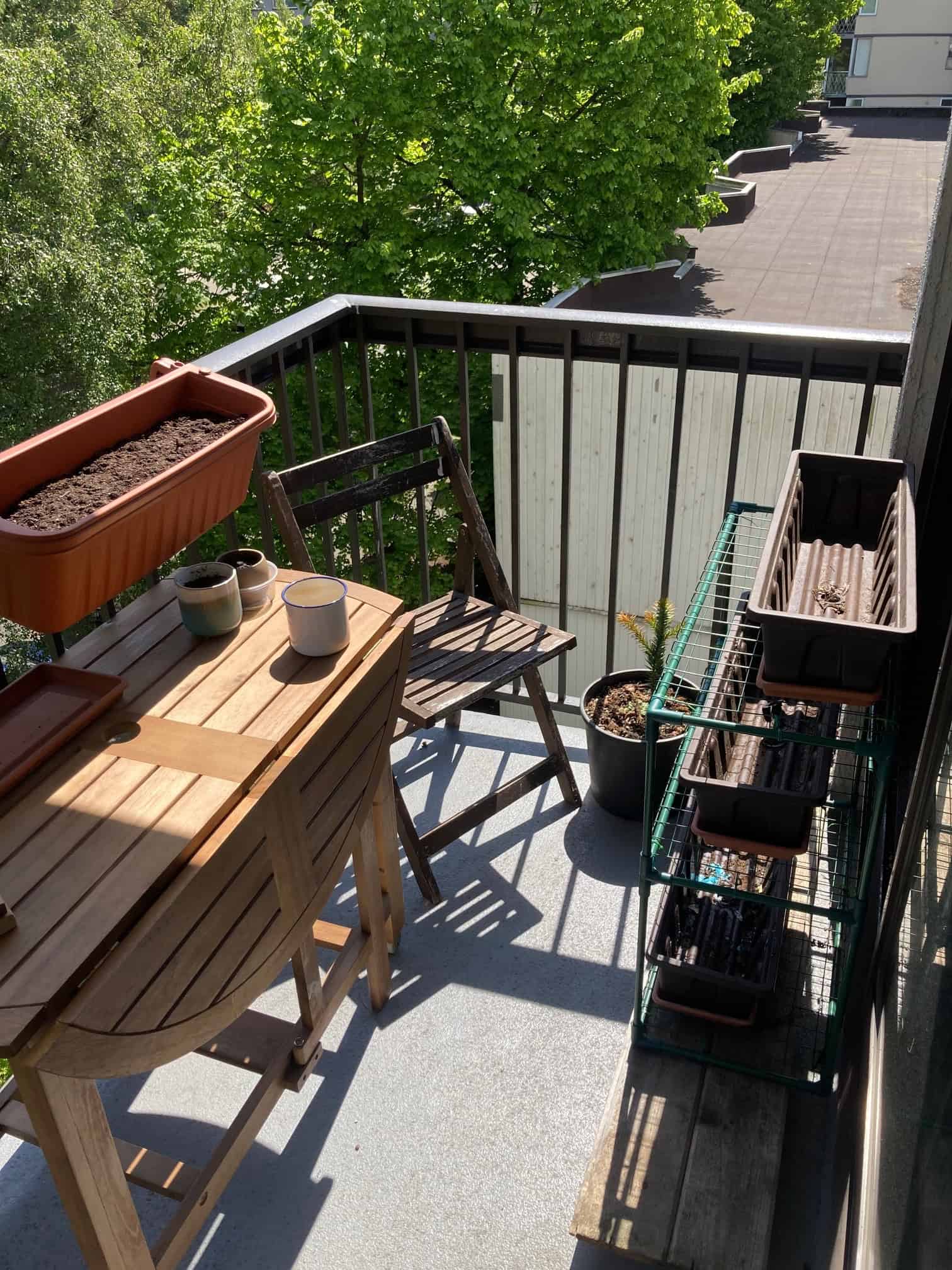 Balcony garden space with wooden table, chairs, planters, and gardening supplies, perfect for outdoor living in Vancouver, BC.
